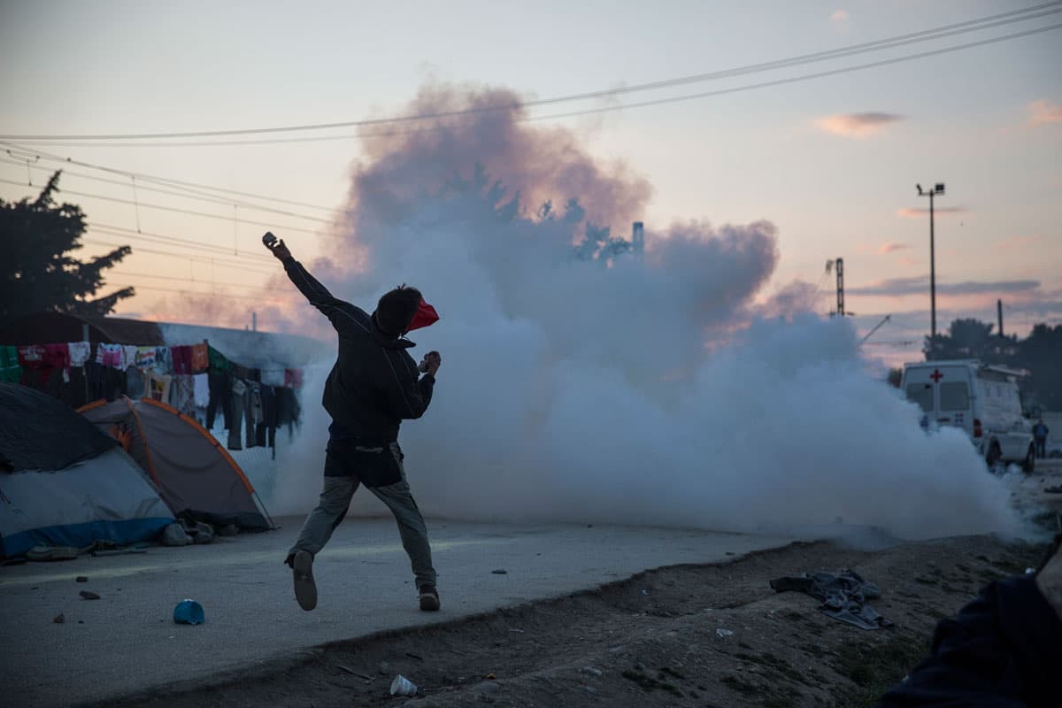 An immigrant throws rocks at Greek police at the Idomeni camp on May 18, 2016. Clashes started when immigrants commandeered an empty train wagon and pushed it toward the Macedonian border. They were stopped by Greek police, who fired tear gas and stun gre