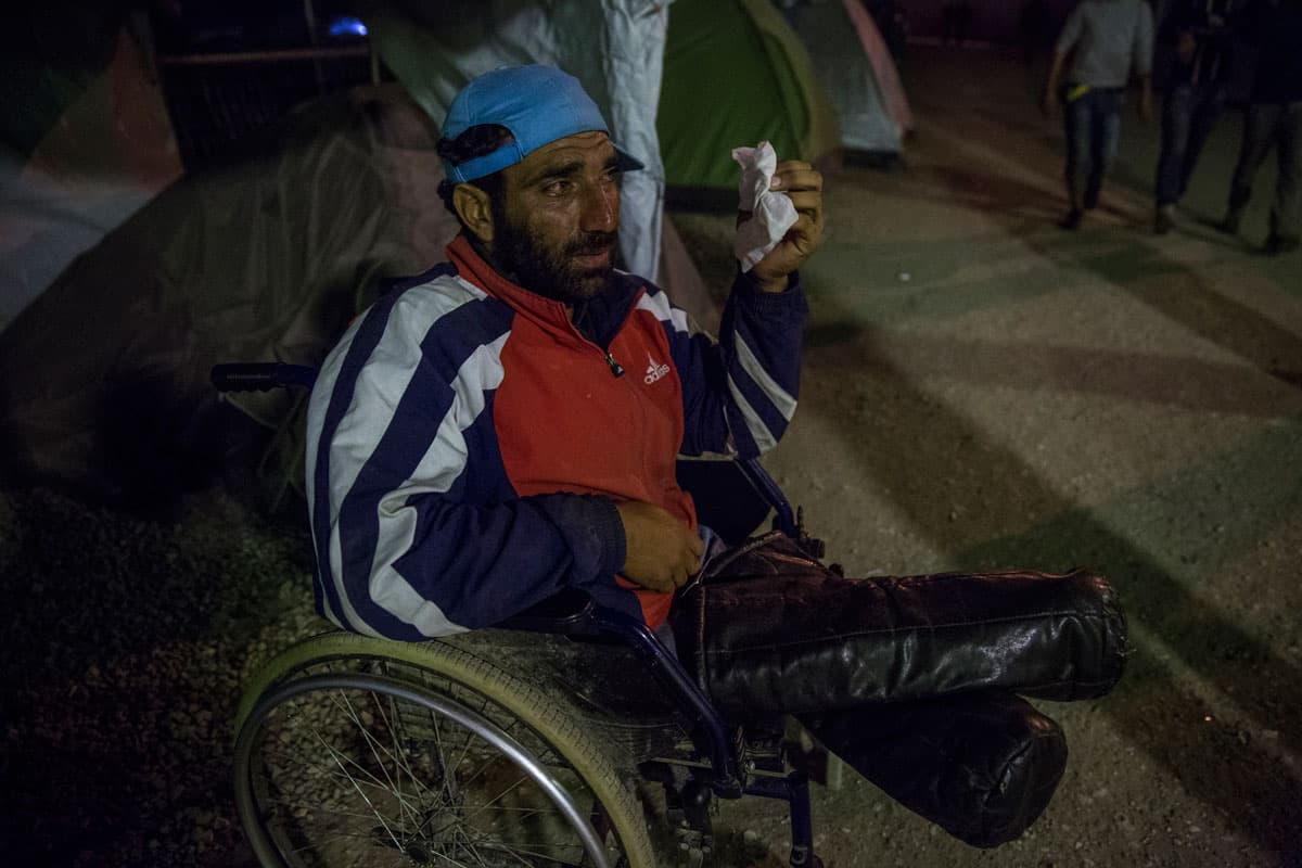 A disabled Syrian refugee wipes his eyes after exposure to tear gas.