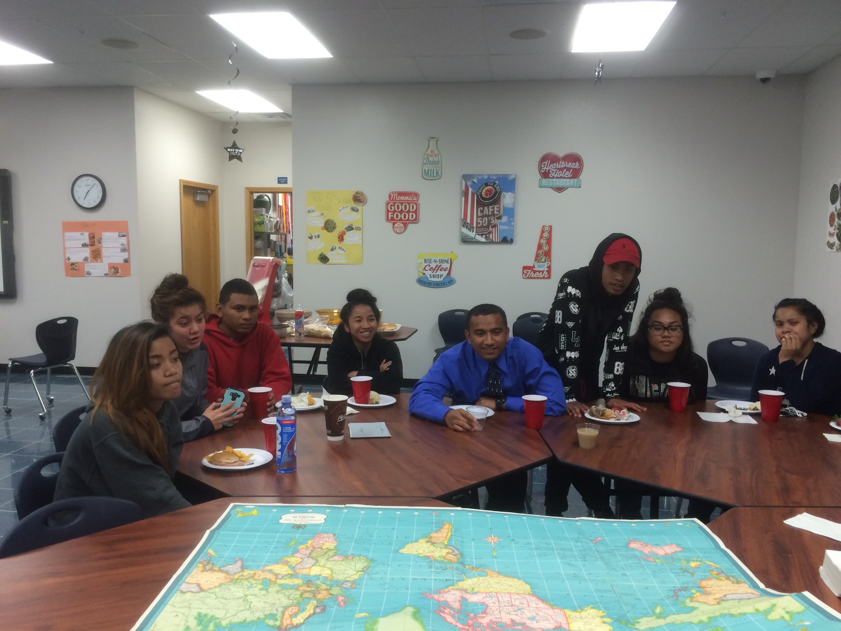 Students sit at a large brown table in front of a map