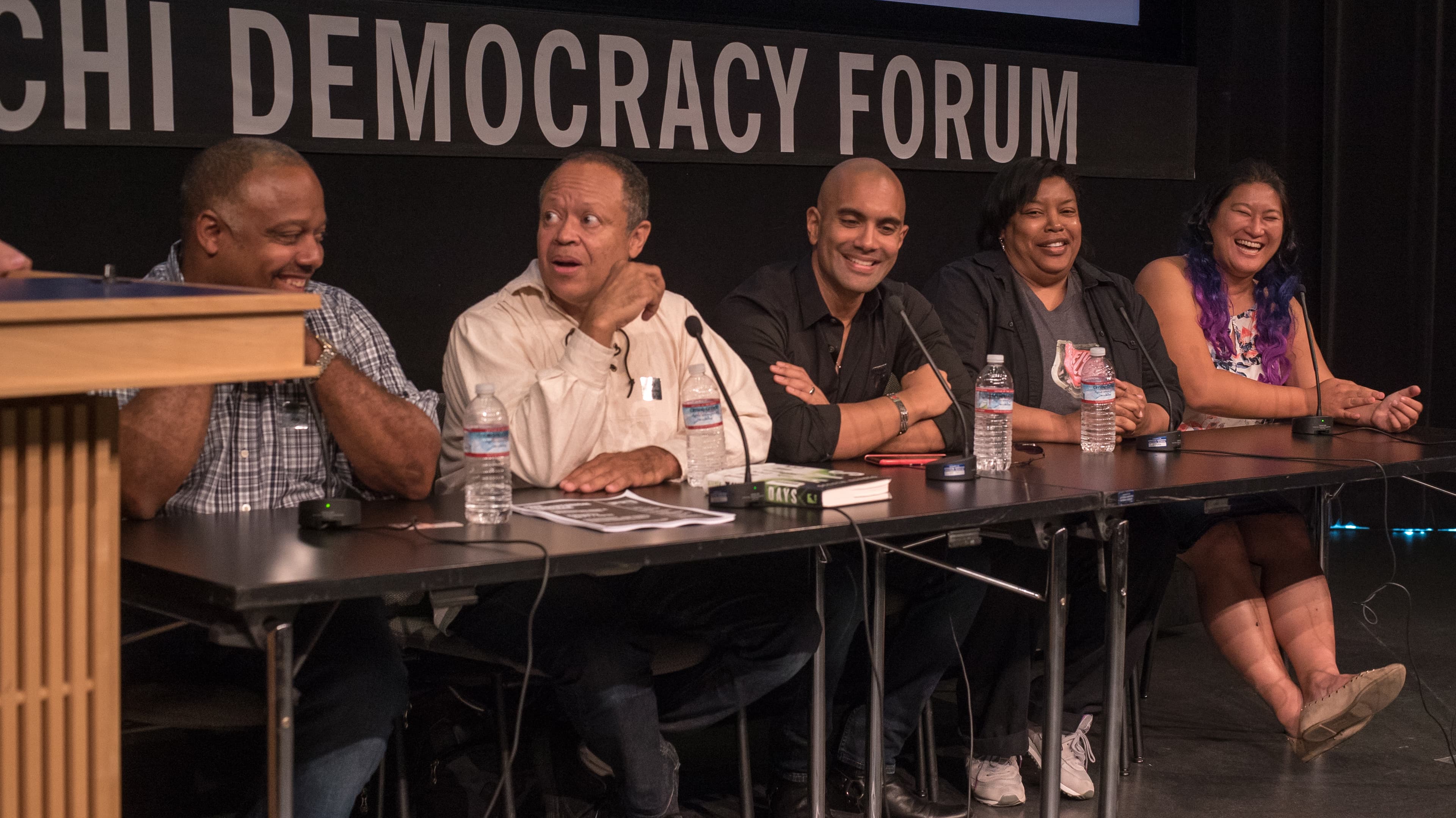 People sitting at table in a row with microphones