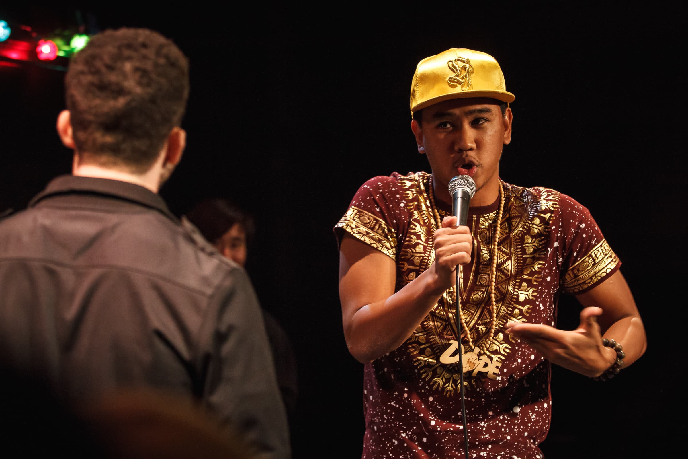 A man is in a face-to-face battle with another performer. He is holding a mic with one hand and gesturing with another.