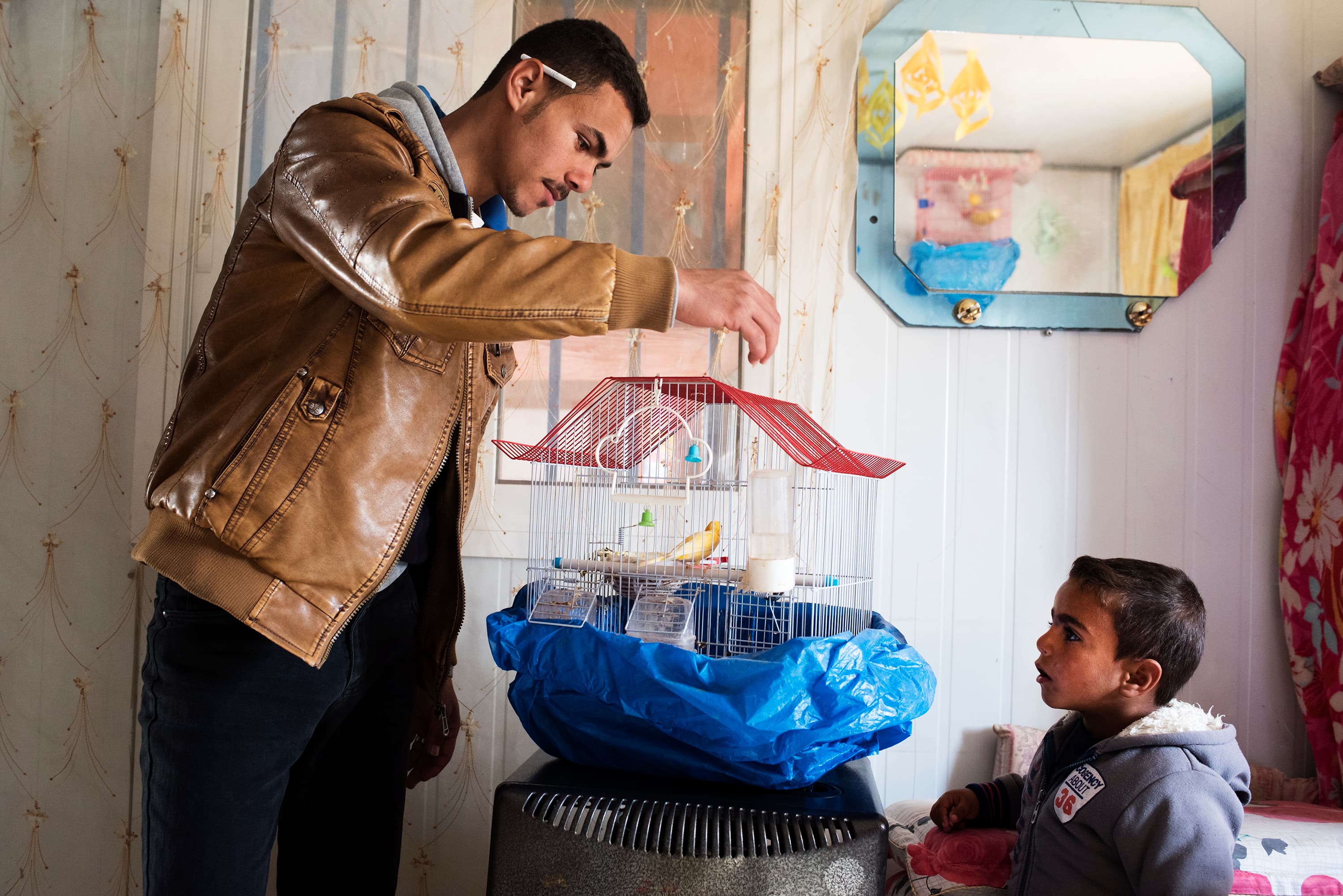 Ala shows off freshly-hatched baby birds to his younger brother Zakaria, 3, in the family's metal shelter.