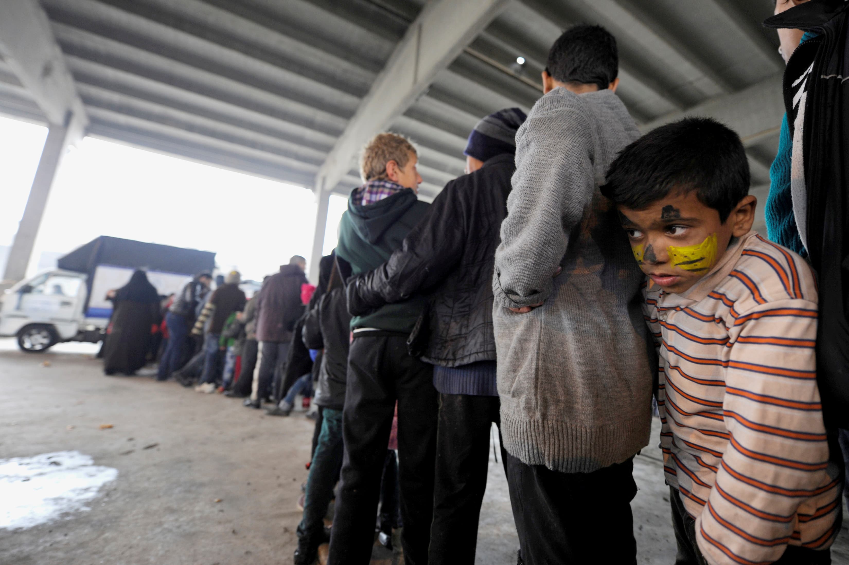 A Syrian boy who has been evacuated from eastern Aleppo, stands in line with a painted face, to receive food aid inside a shelter in government controlled Jibreen area in Aleppo.
