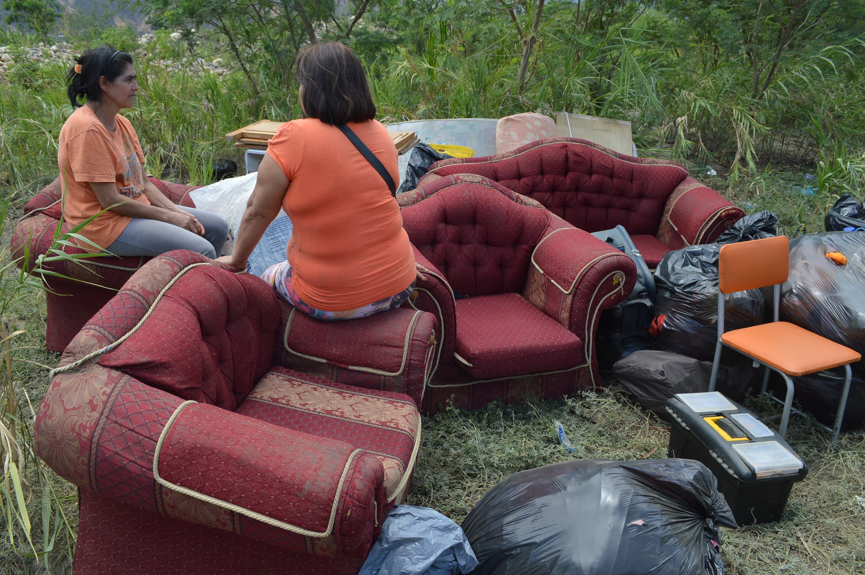 Women sit on red sofa chairs in a field.