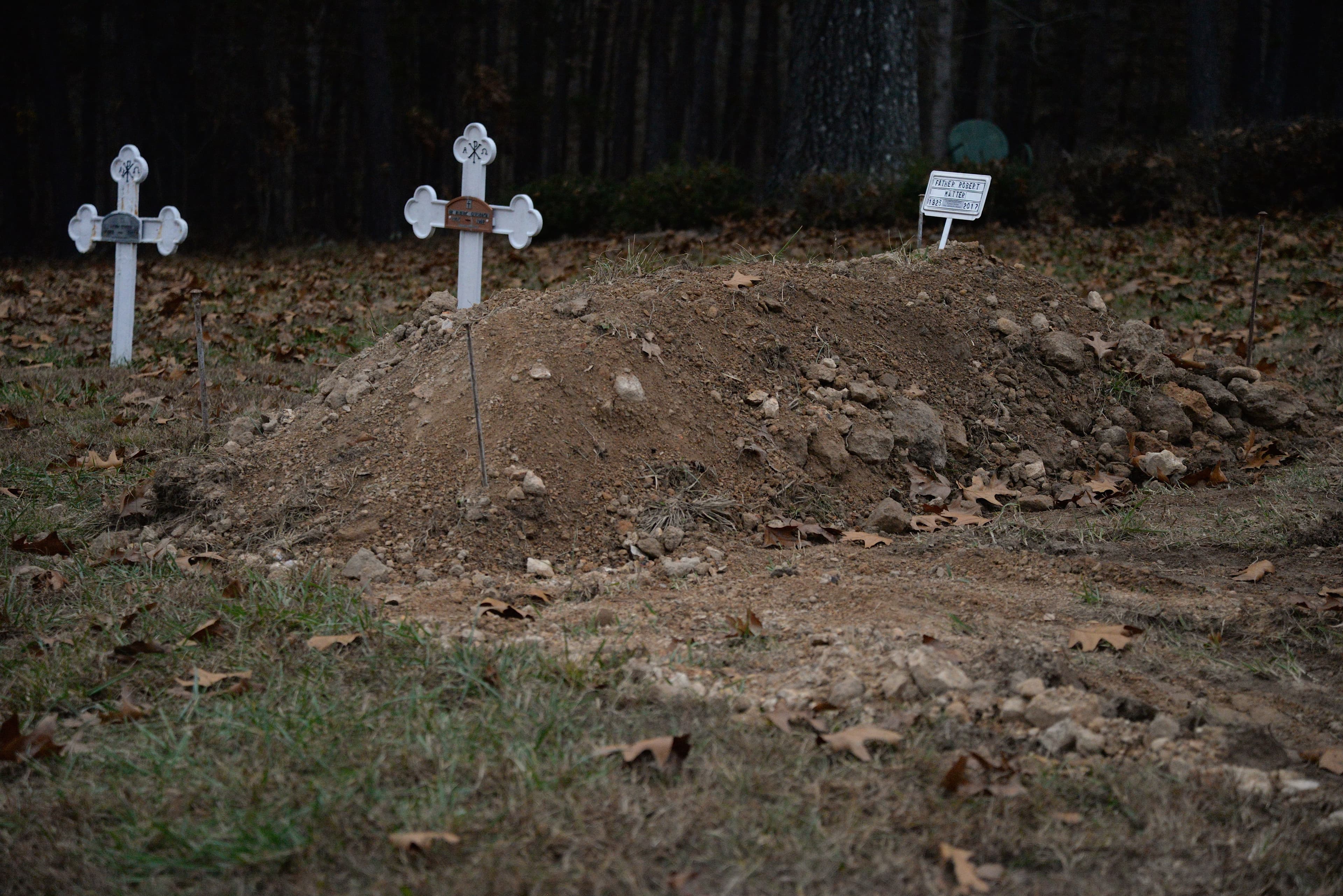 Fresh grave, mound of diret with cross at top. Other white crosses nearby.