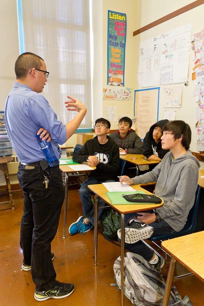 Teacher speaks in front of group of students at their desks