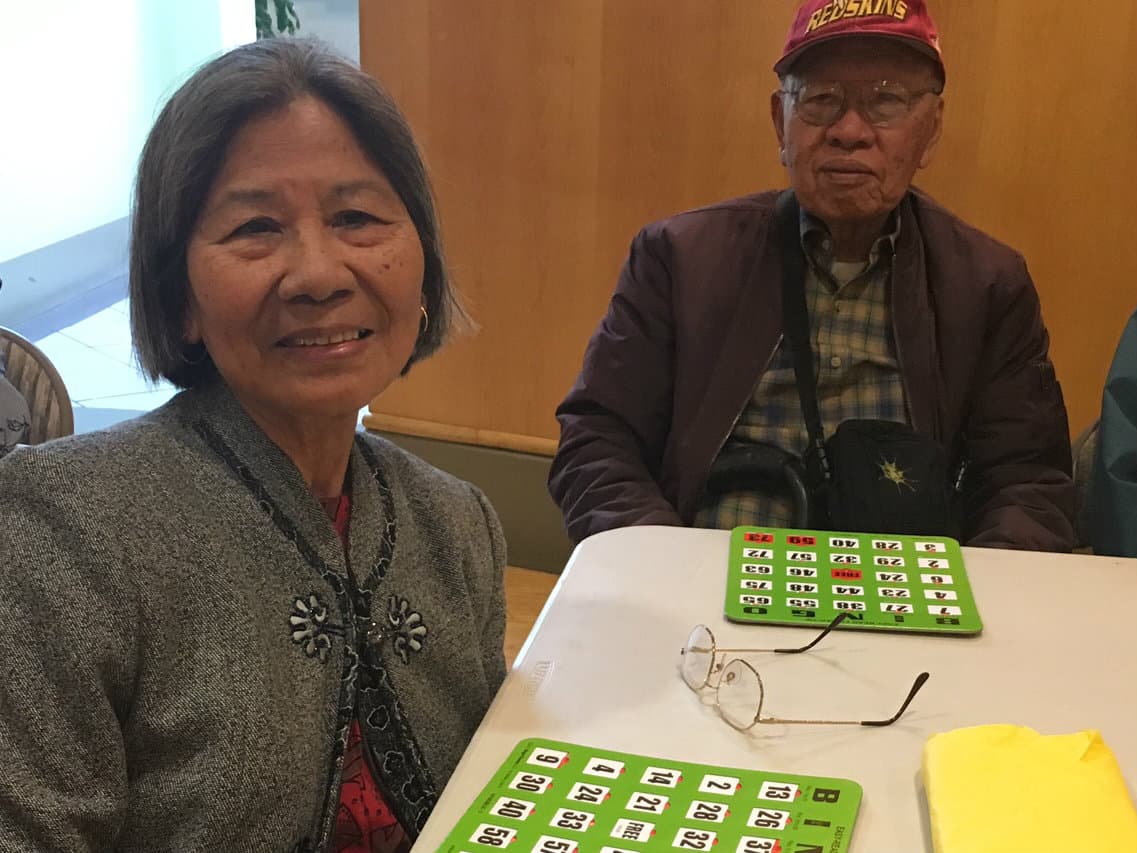 Woman in foreground, man in background sitting at a table and looking at camera