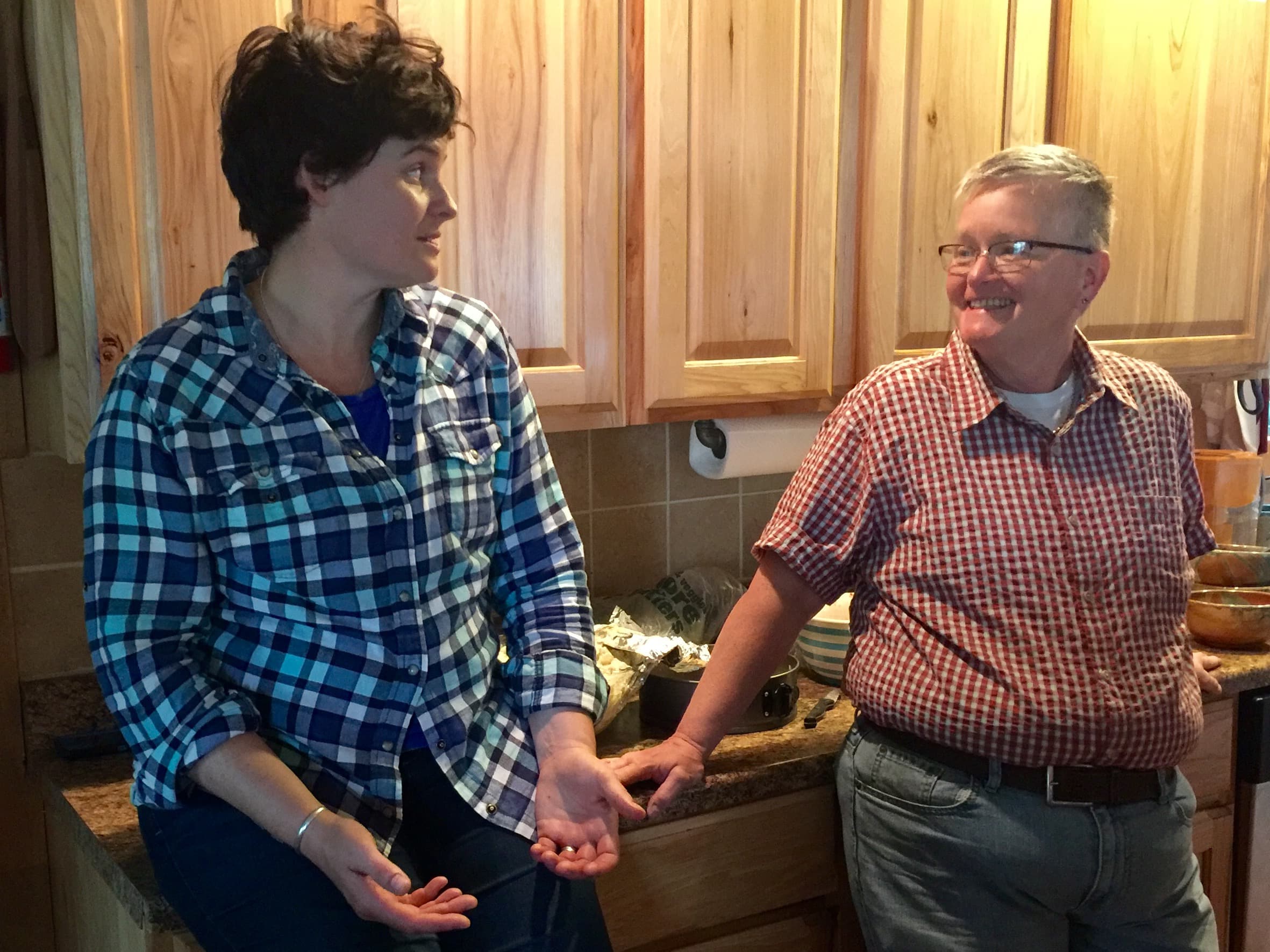 Poole stands facing Taylor with back to wooden cabinets