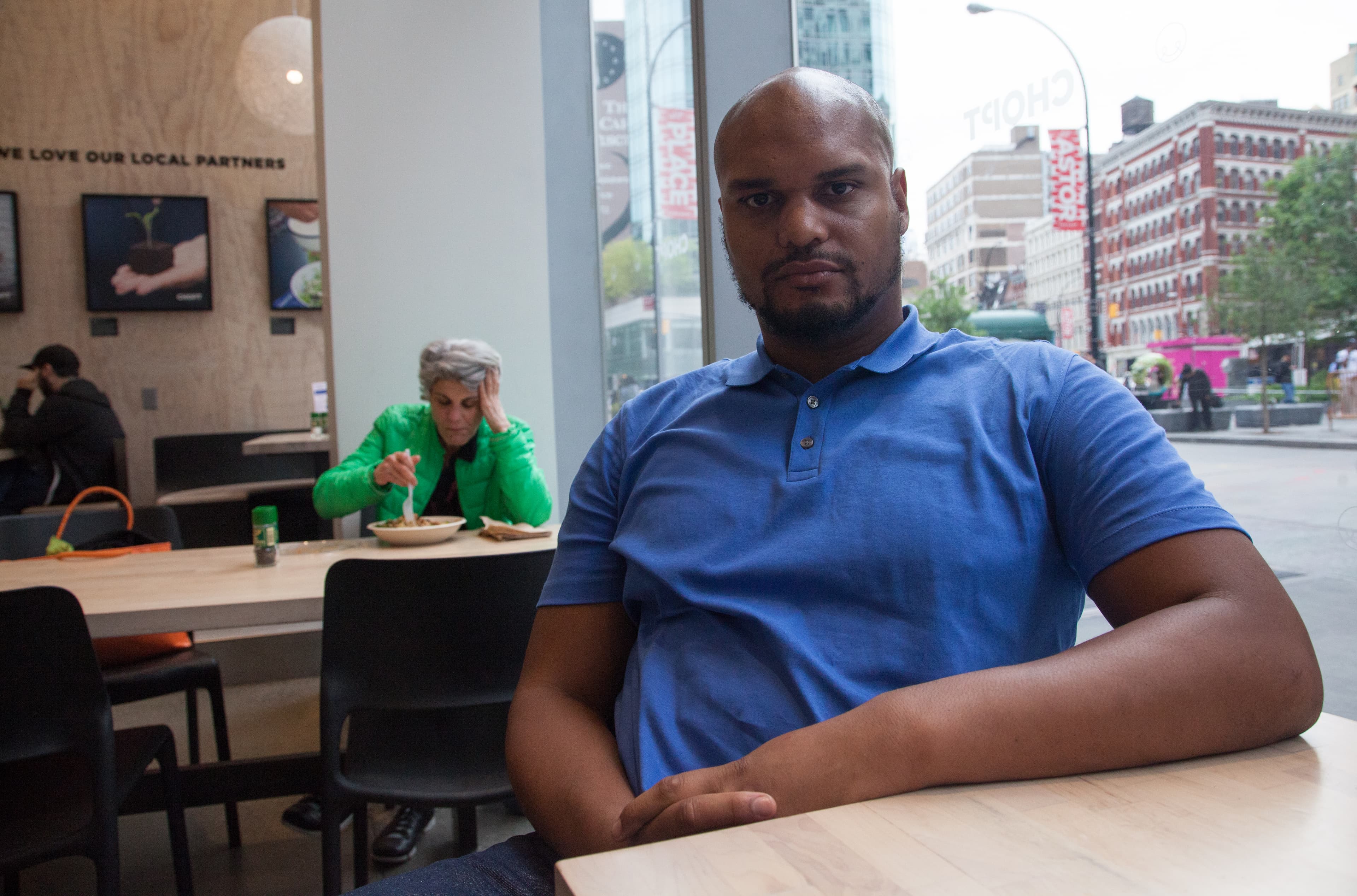 Man sitting at table with cup of coffee, cafe windows looking out to the street behind him