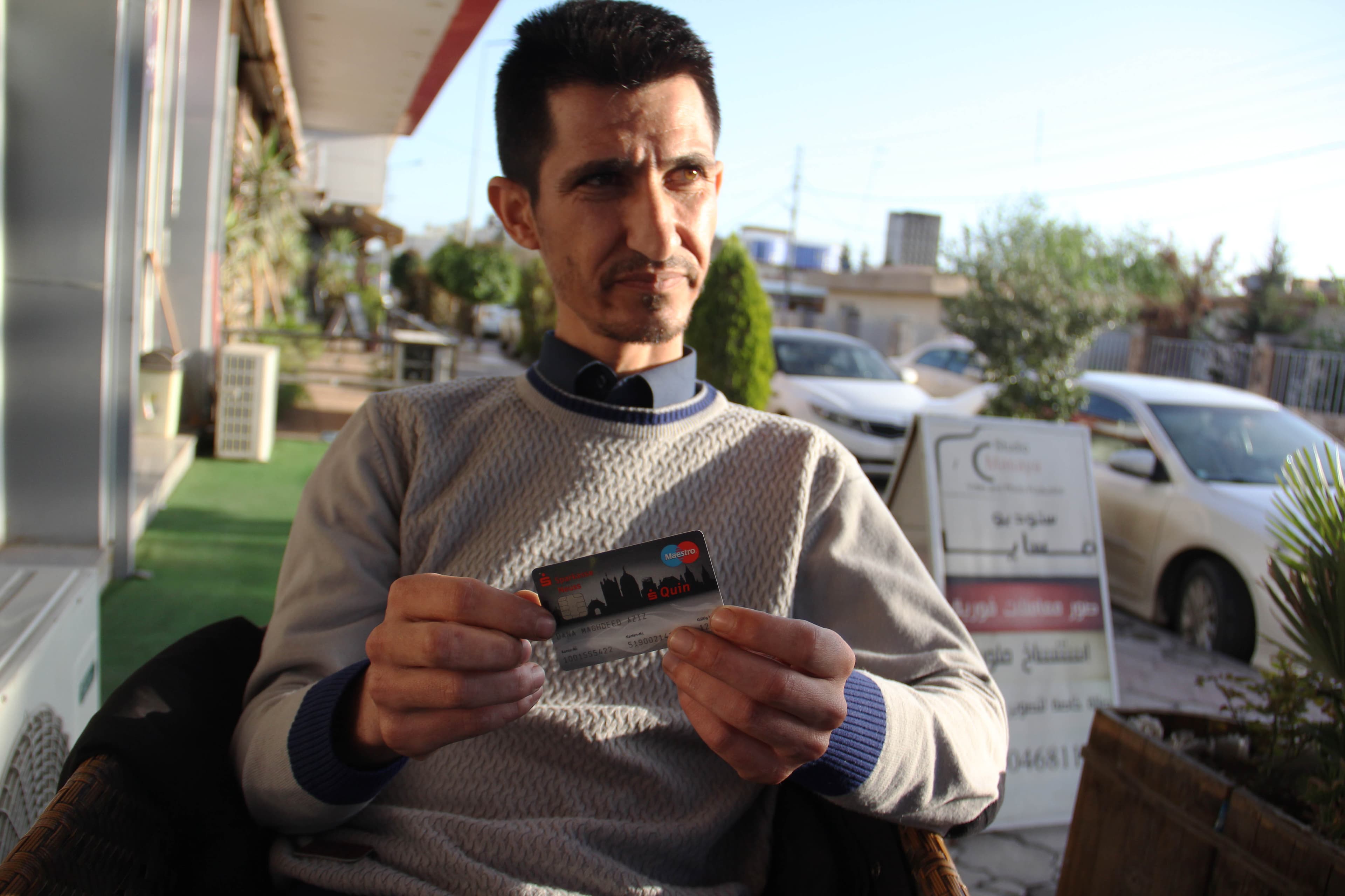 Dana Maghdeed Aziz holds up the cards through which he received a stipend from the Germany government.