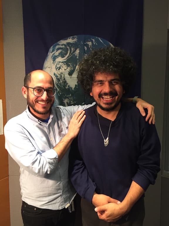 Two men stand smiling in front of a picture of the world.