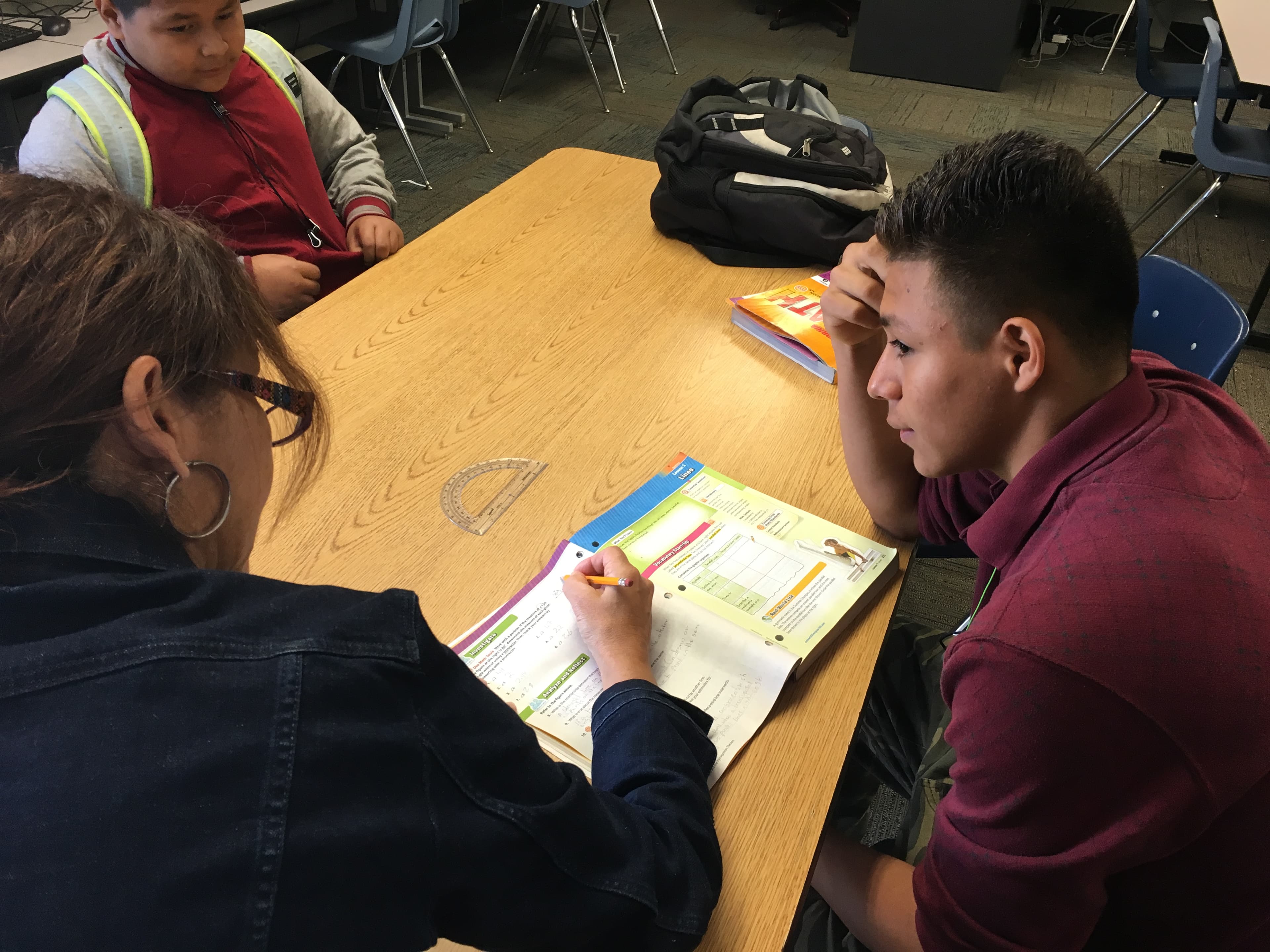 Boy at desk looks at adult who is writing in notebook