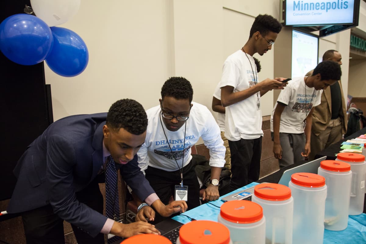 Two men at end of table hunch over a computer