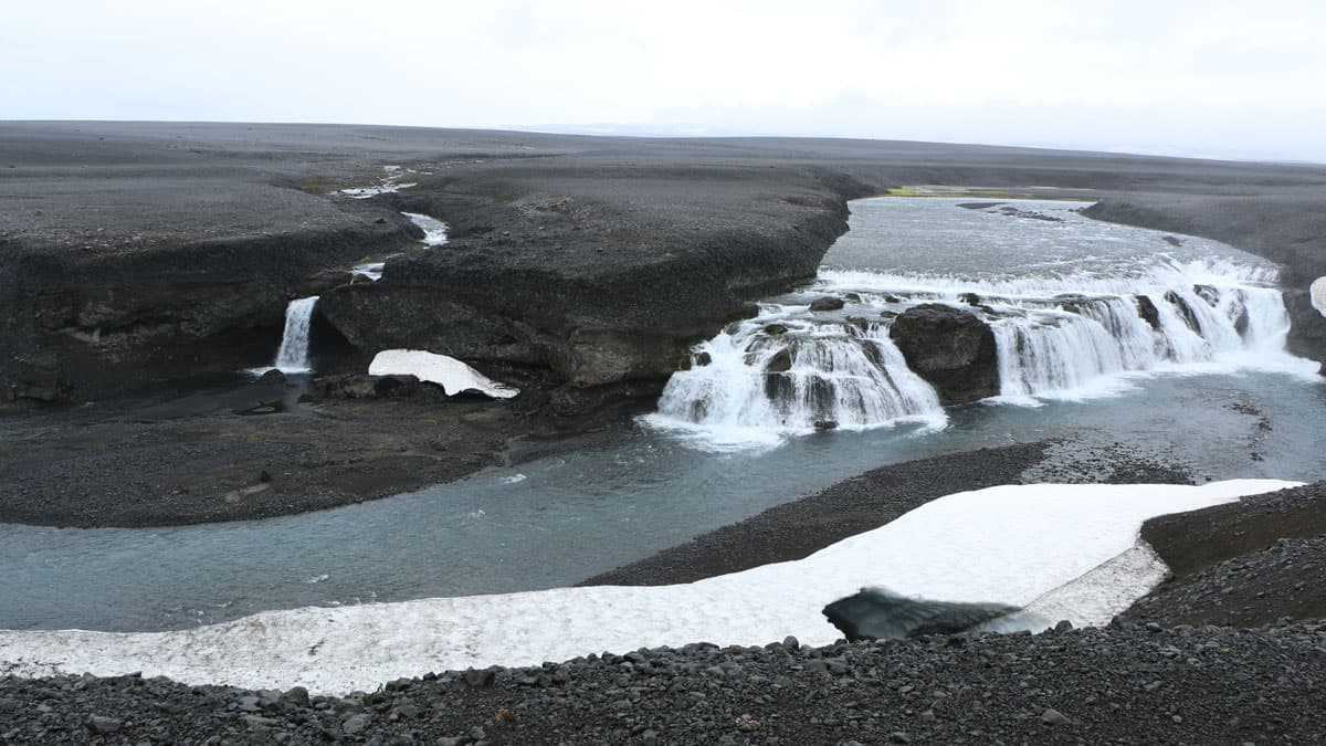 A waterfall cascades in an otherwise desolate volcanic landscape.