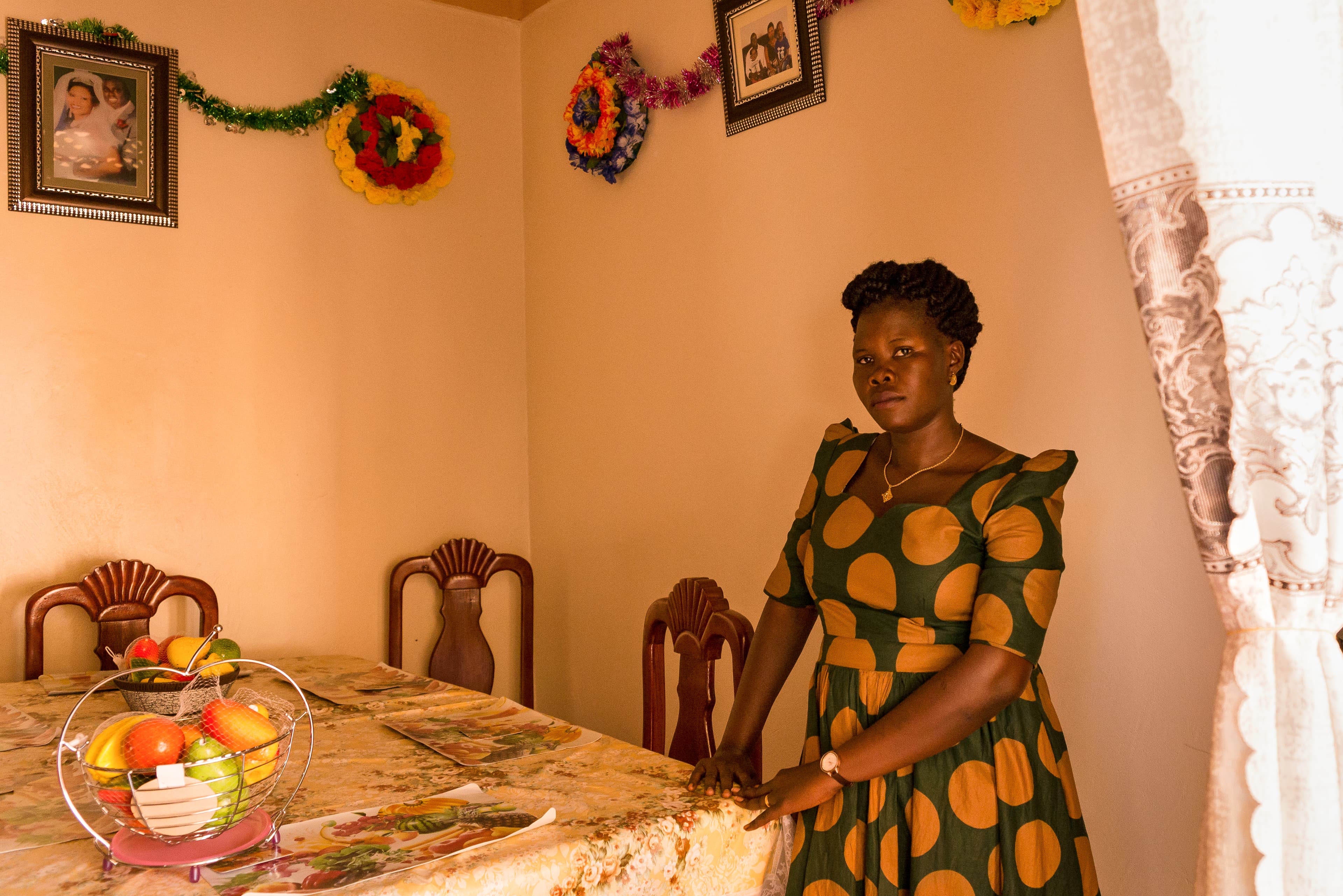 Lika, 29, stands at a dining room table in her home in northern Uganda.