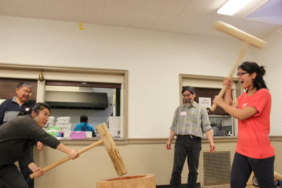 Two young women swinging large hammer into wooden bowl