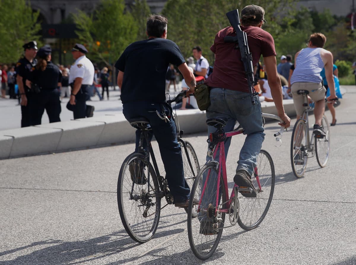 A man rides on his bike with a gun over his shoulder at public square outside the RNC.