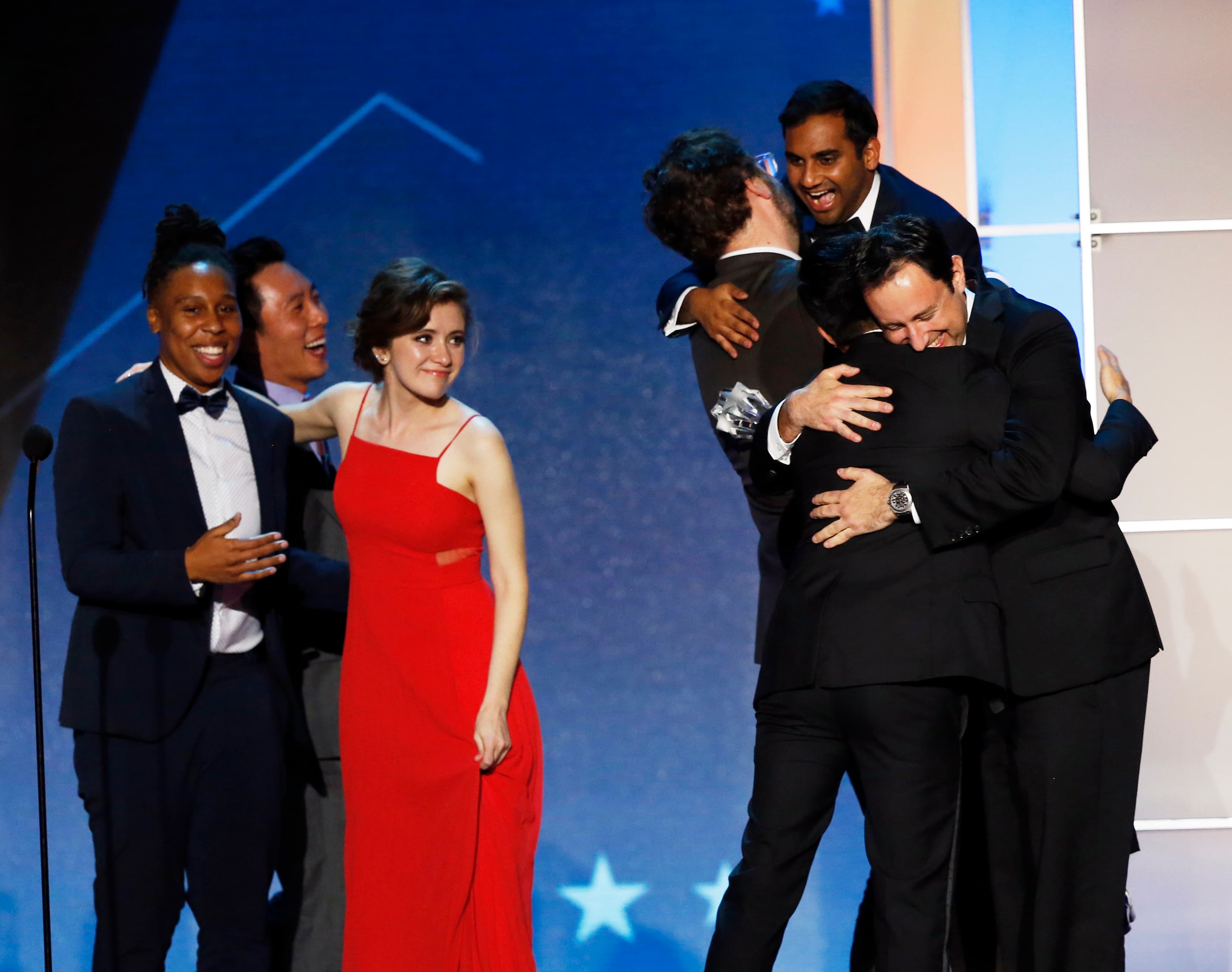 Group on stage hugging, with Ansari lifted up