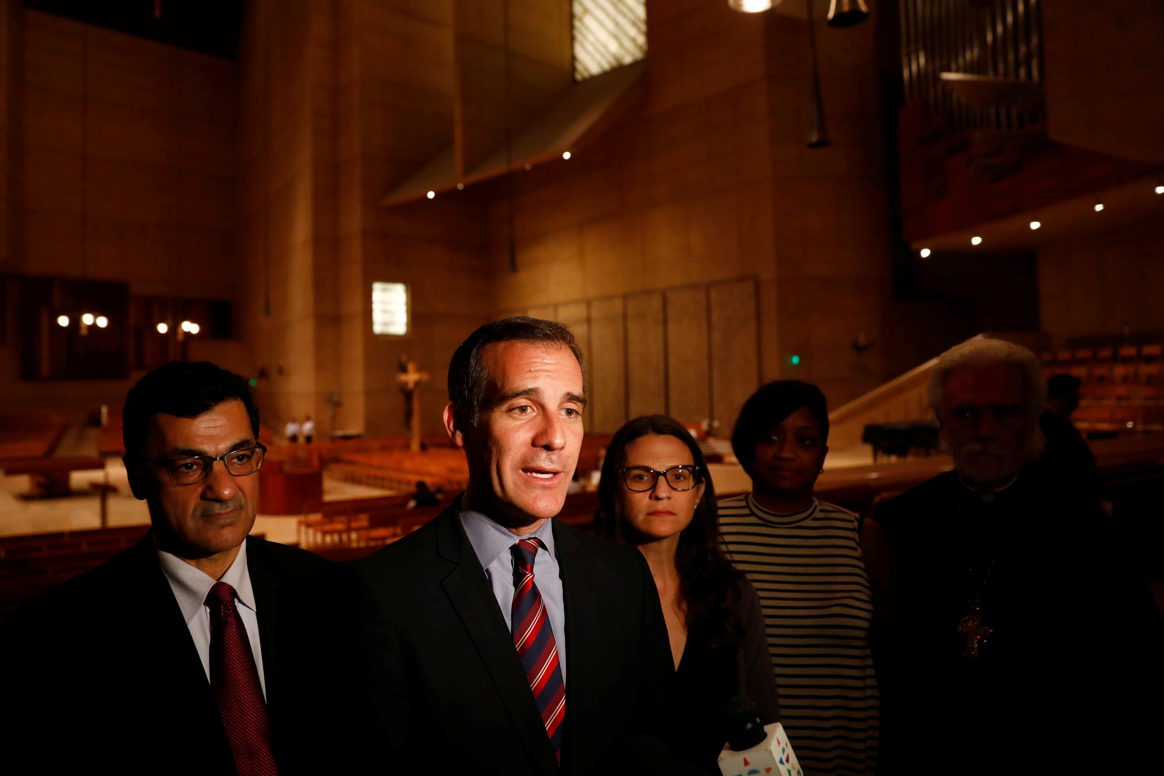 Man in suit speaking, with two people behind him