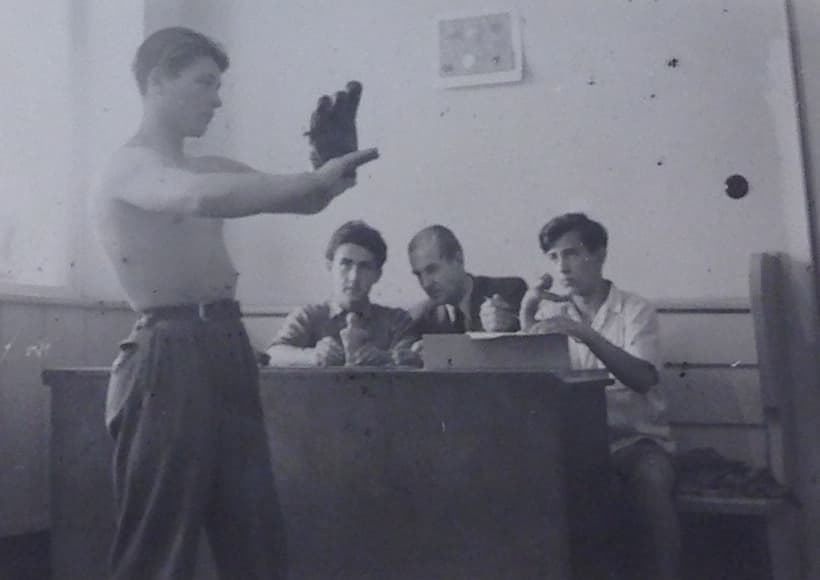 A shirtless young man poses with a baseball mitt for two children and their instructor during a sculpture class