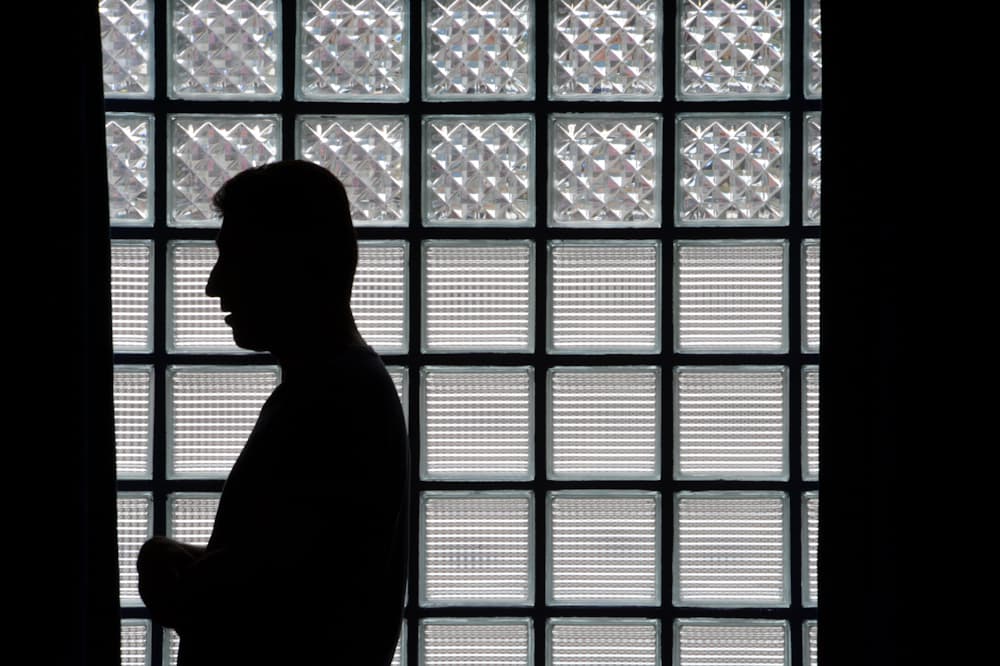 A Muslim man is praying behind thick glass and heavy curtains at Al Taqua prayer space in the Metaxourgio neighborhood.