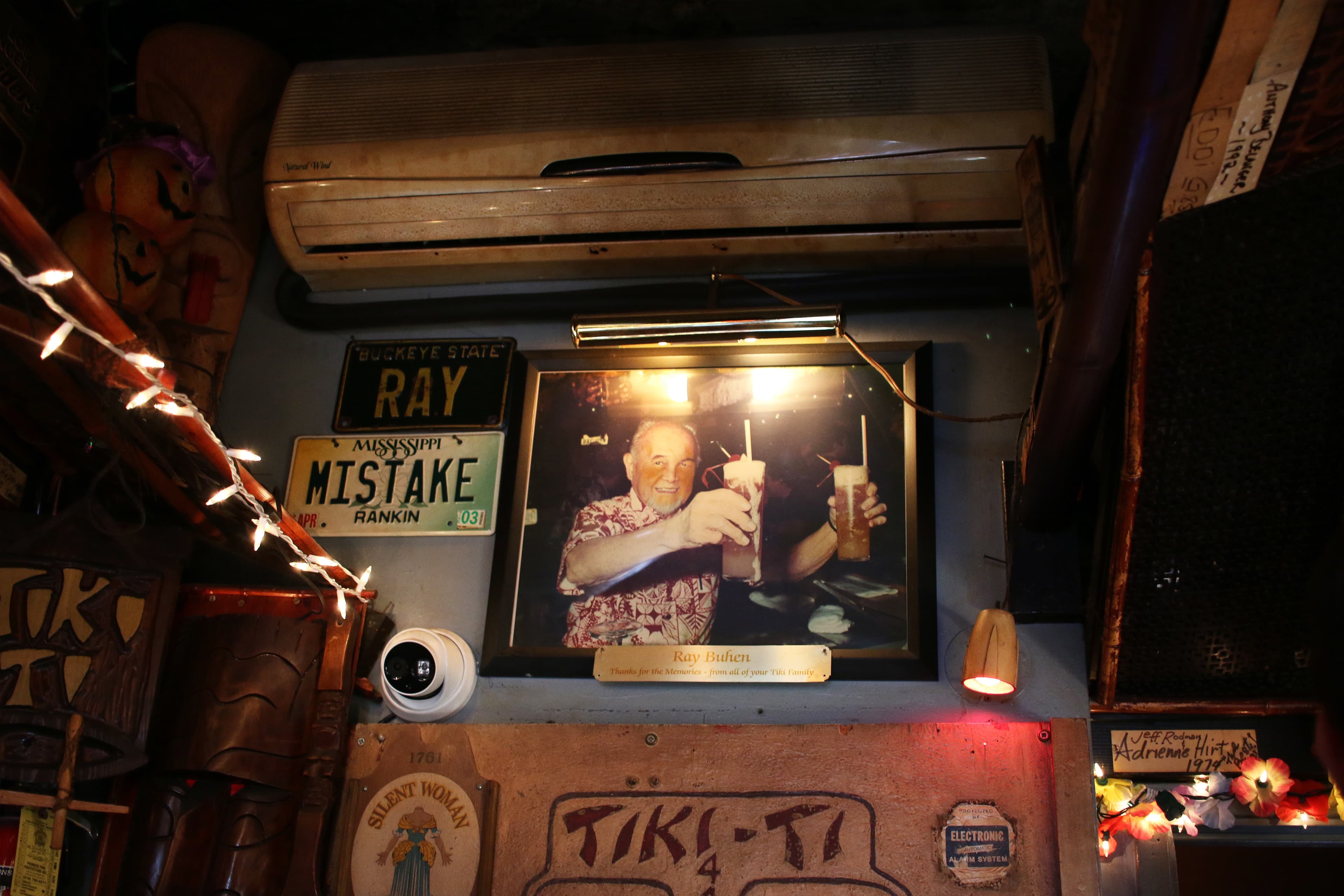 Photo near ceiling, with streamers shows elderly man holding up two colorful drinks and smiling