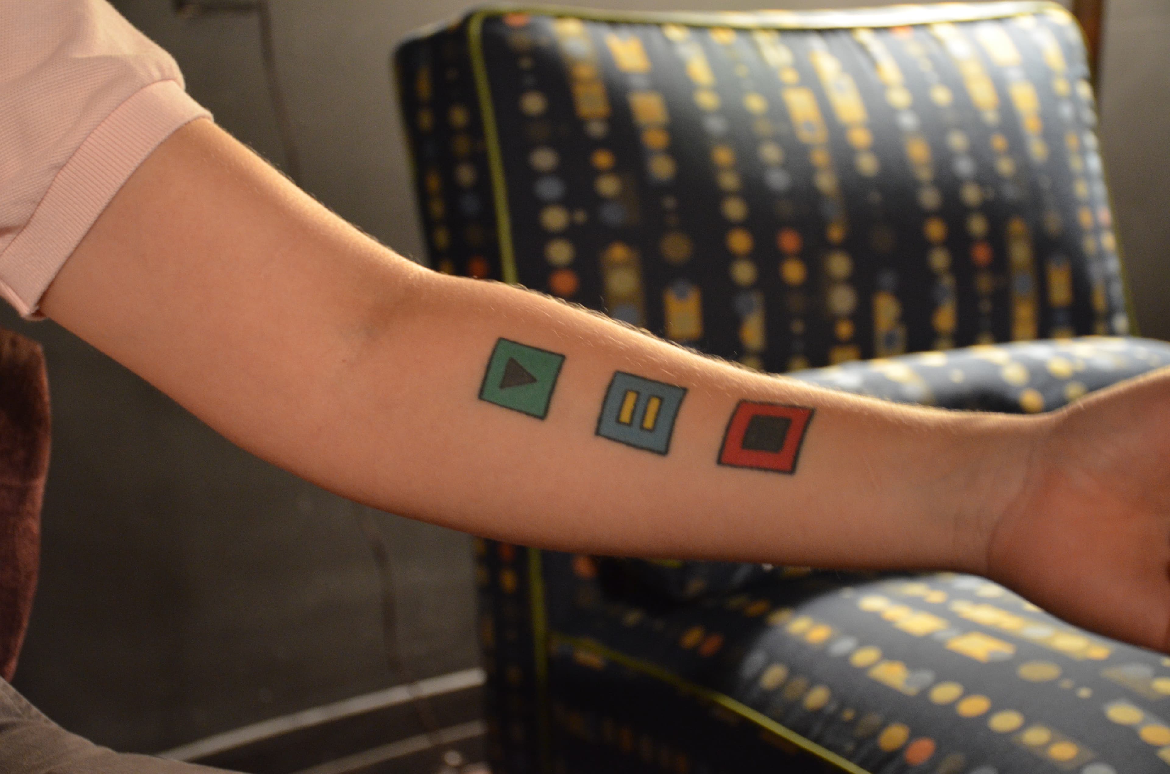 AJ's tattoo of play, pause and stop buttons, includes the LGBT equality symbol.