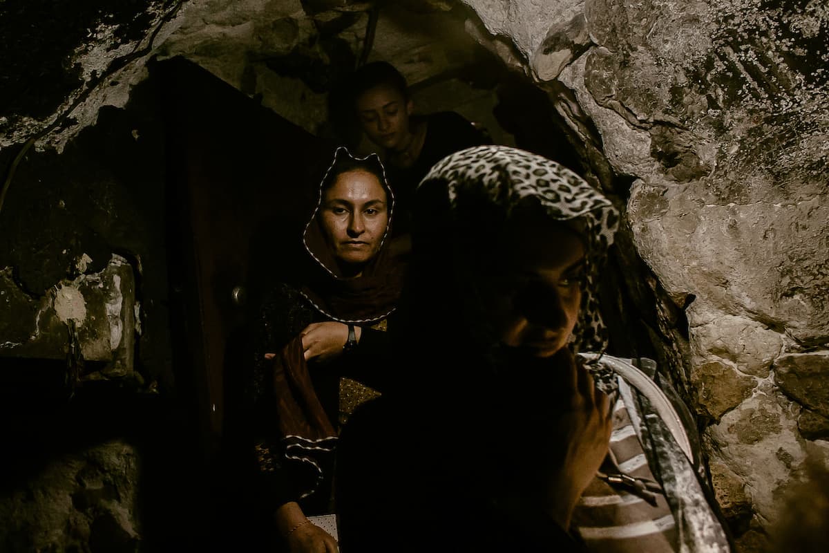 Ghazal Naser Khalaf (center) and Turkia Hussein (right) descend through a narrow entrance leading to a sacred fountain.