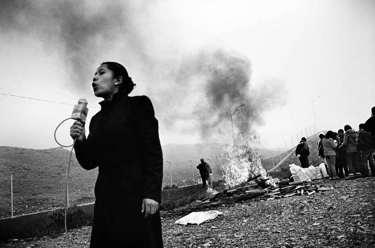 A Bolivian television journalist stands in front of the burning remains of a large drug seizure by anti-narcotics agents in February 2008.