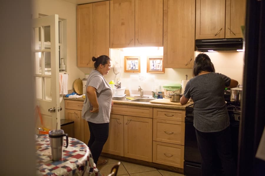 Two woman standing at counter in kitchen, photographed through doorway behind them