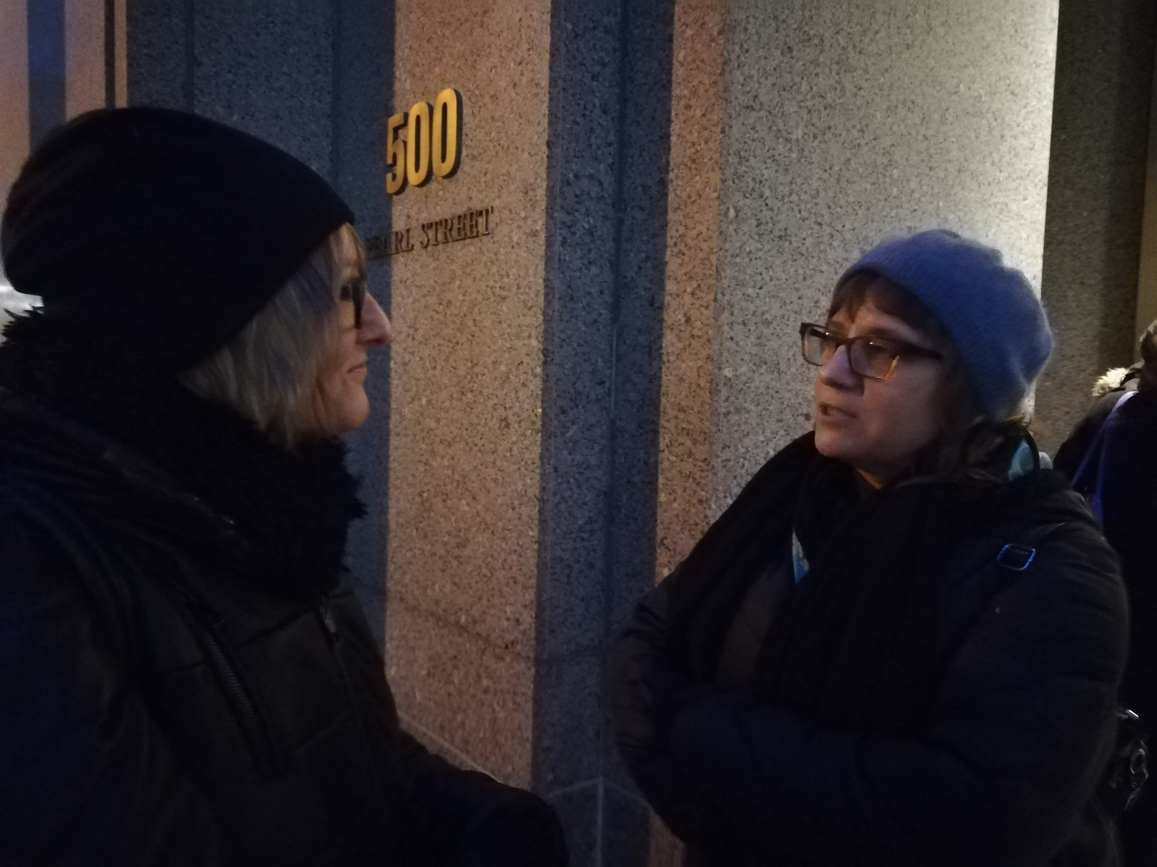 Two women stand in front of building, talking to each other