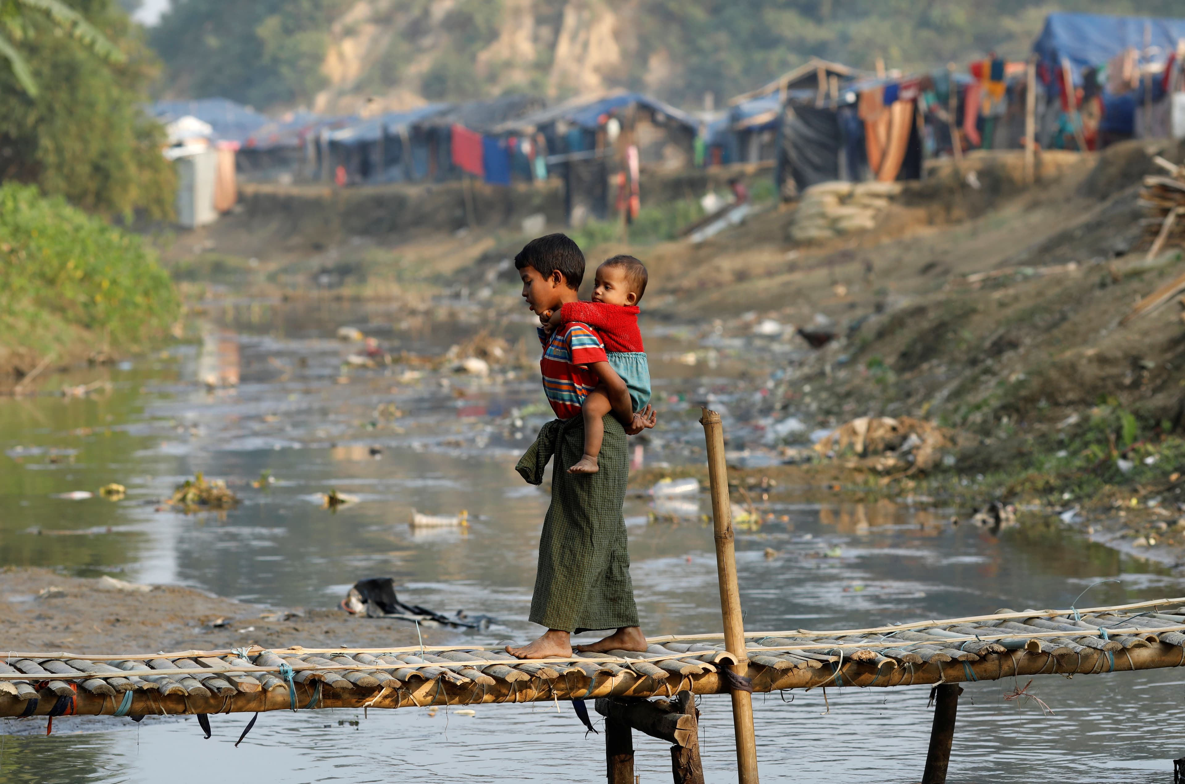 A Rohingya refugee child, carrying another child, walks along a bridge from no-man's land to Bangladesh, at the Bangladesh-Myanmar border near Cox's Bazar, Bangladesh, Jan. 12, 2018.