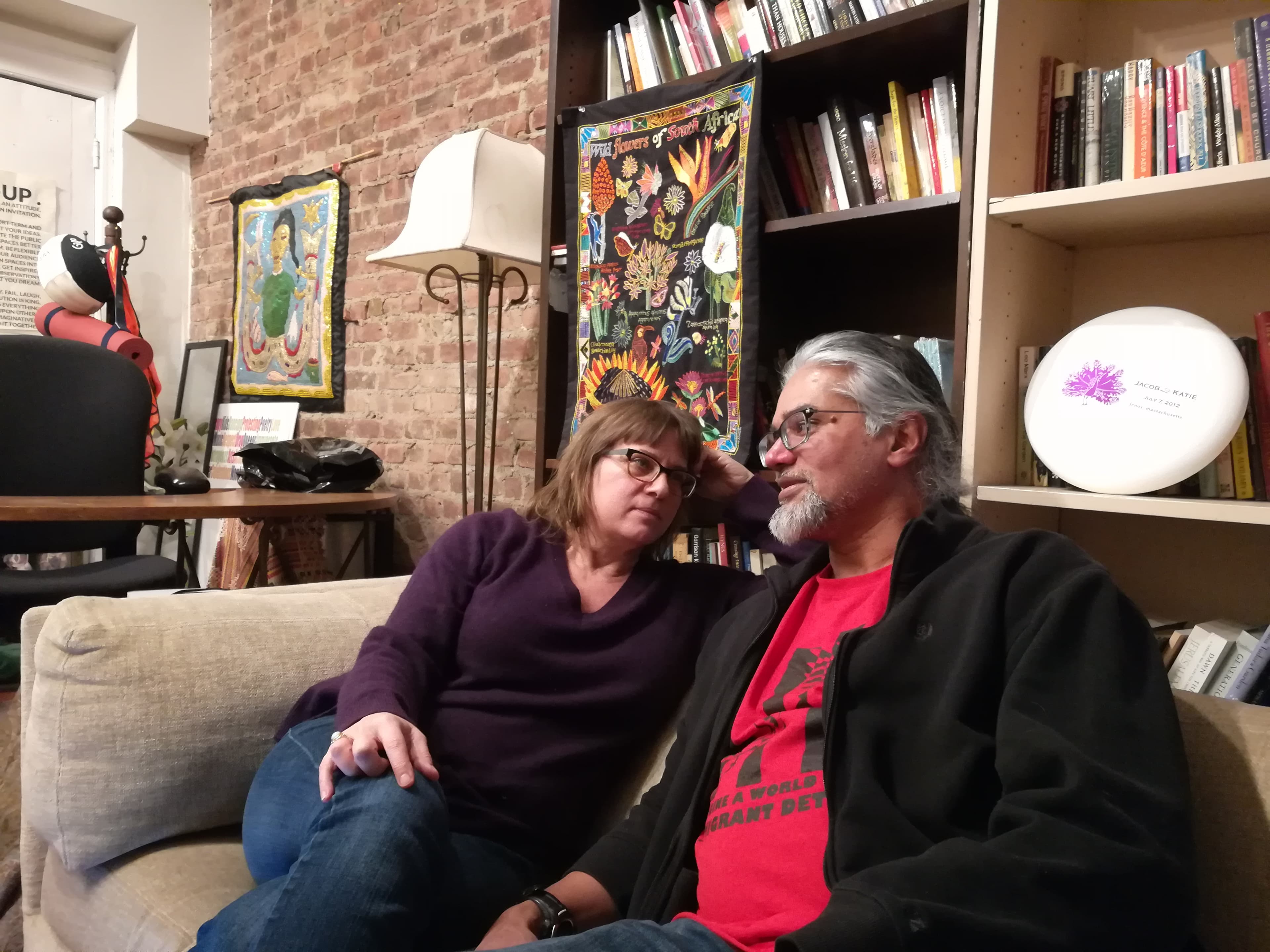 Woman sitting on sofa in front of bookshelf, looking at man