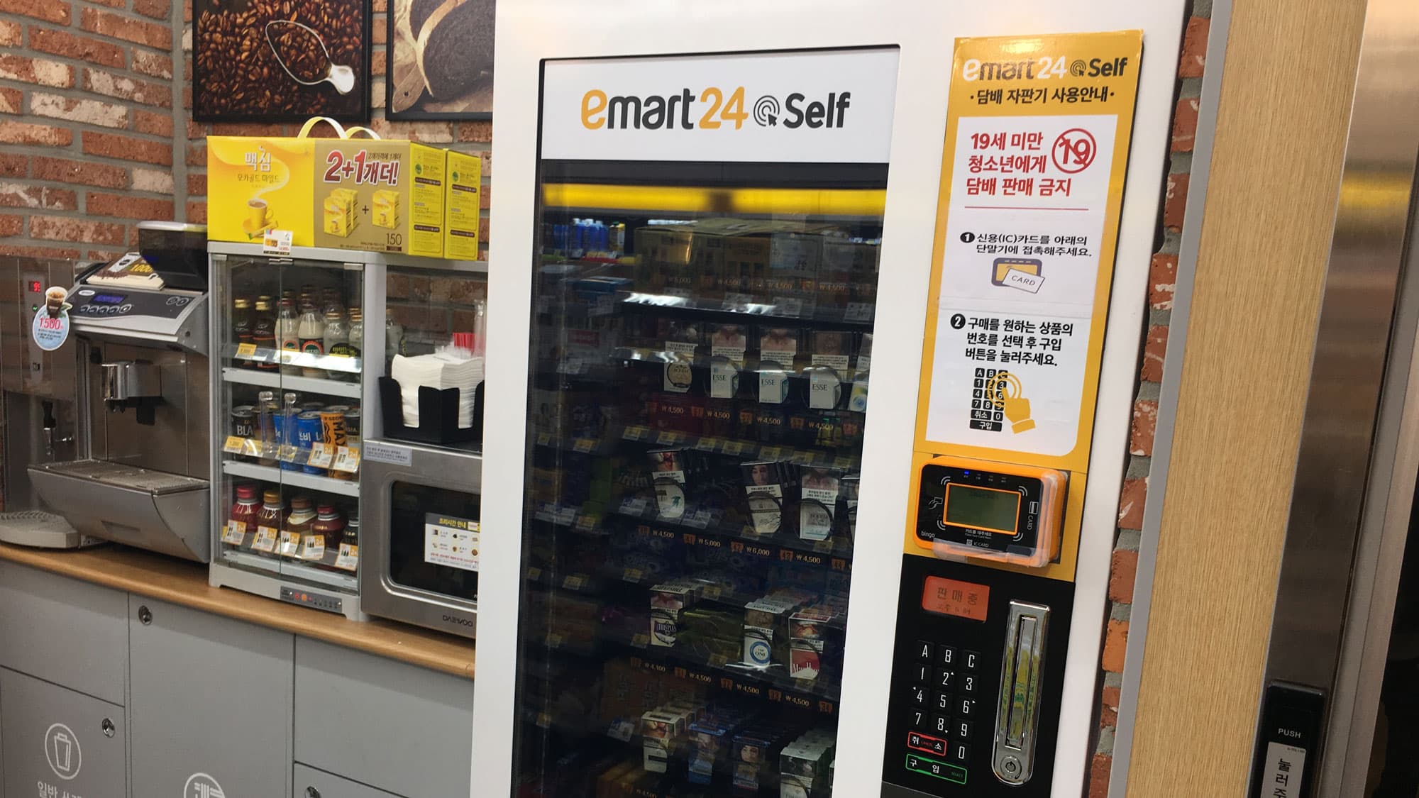 A kiosk holds packs of cigarettes behind glass. At the right, is a credit card reader and instructions in Korean.