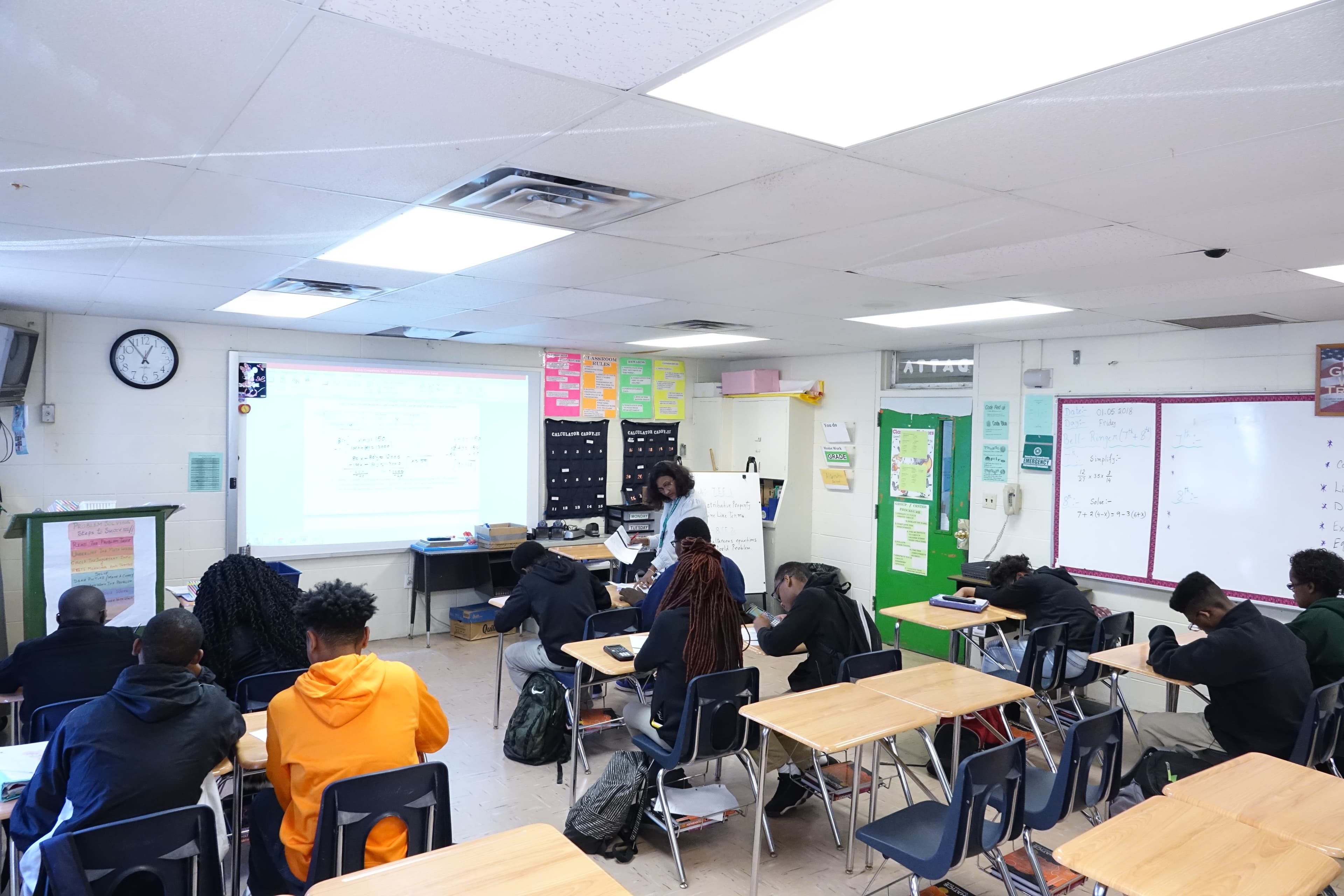 Wide view of classroom with students sitting at desk, teacher at front of room