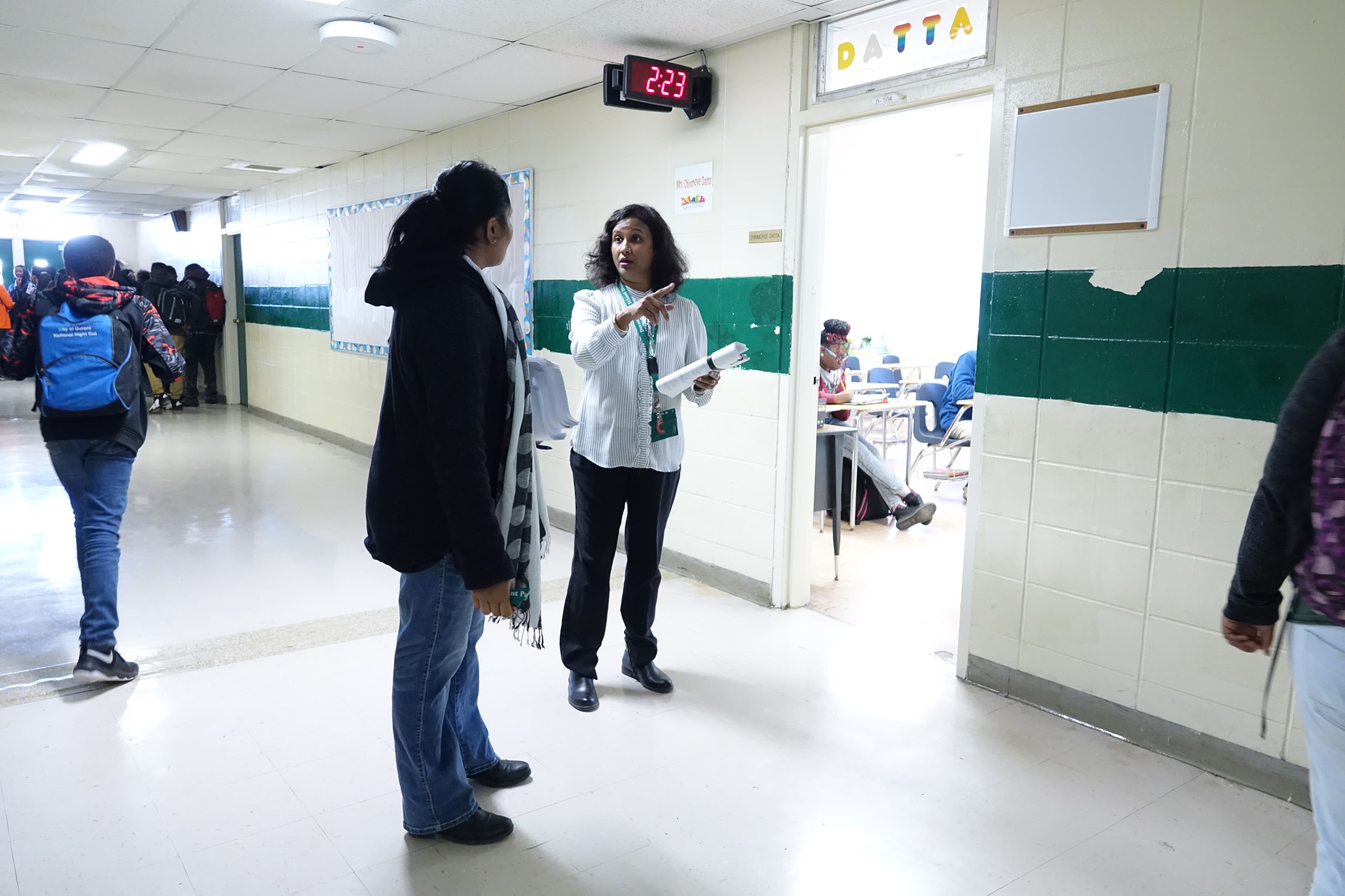 Woman in school hallway points while talking to a student