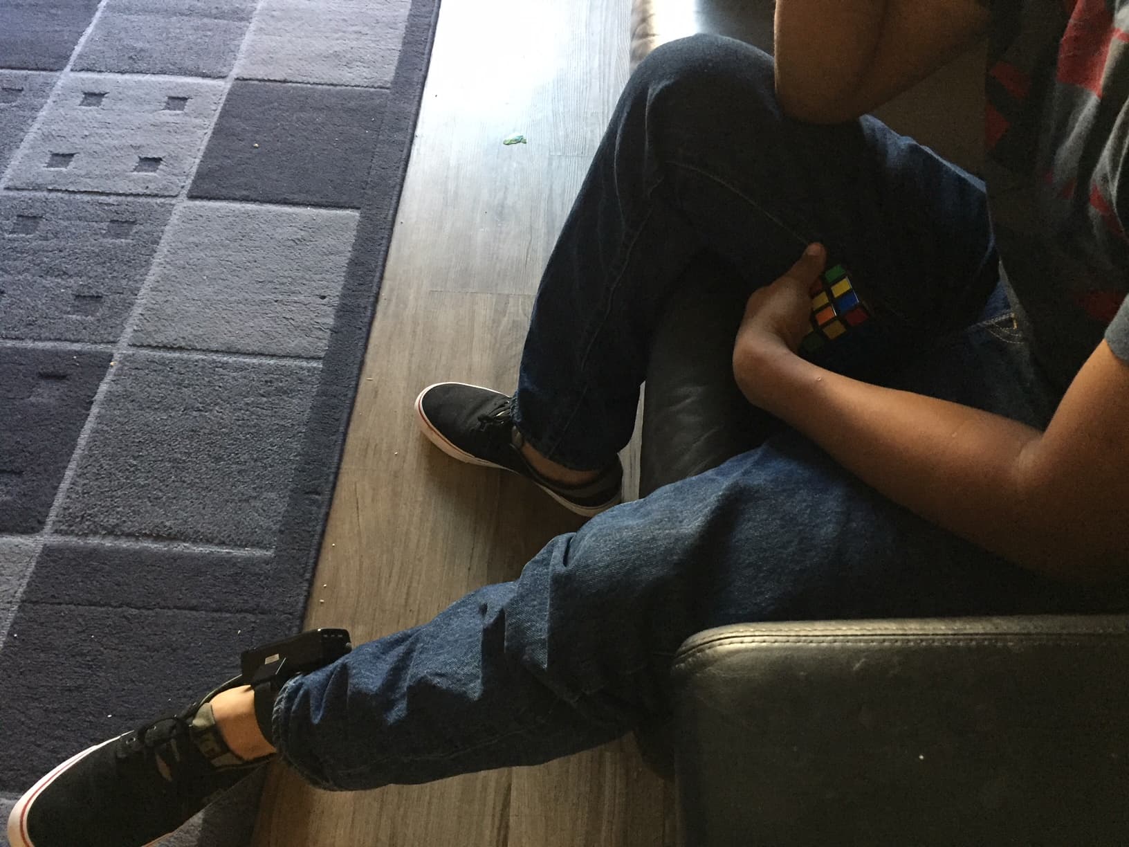 Man's legs, monitoring device around his ankle, sitting on sofa