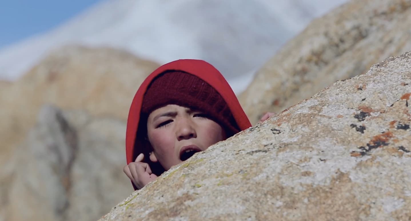 The rinpoche hides behind a boulder as his friend lights firecrackers.