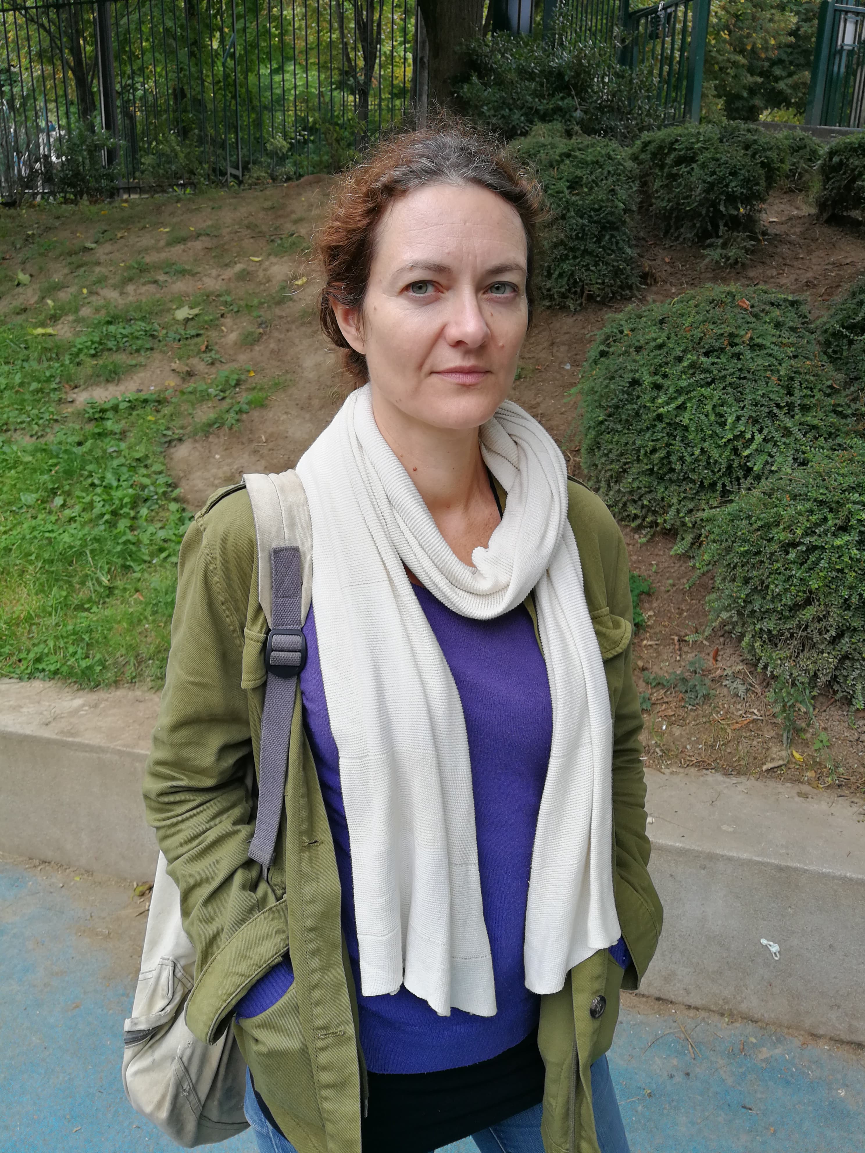 A woman stands outside looking straight at the camera with a serious expression on her face.