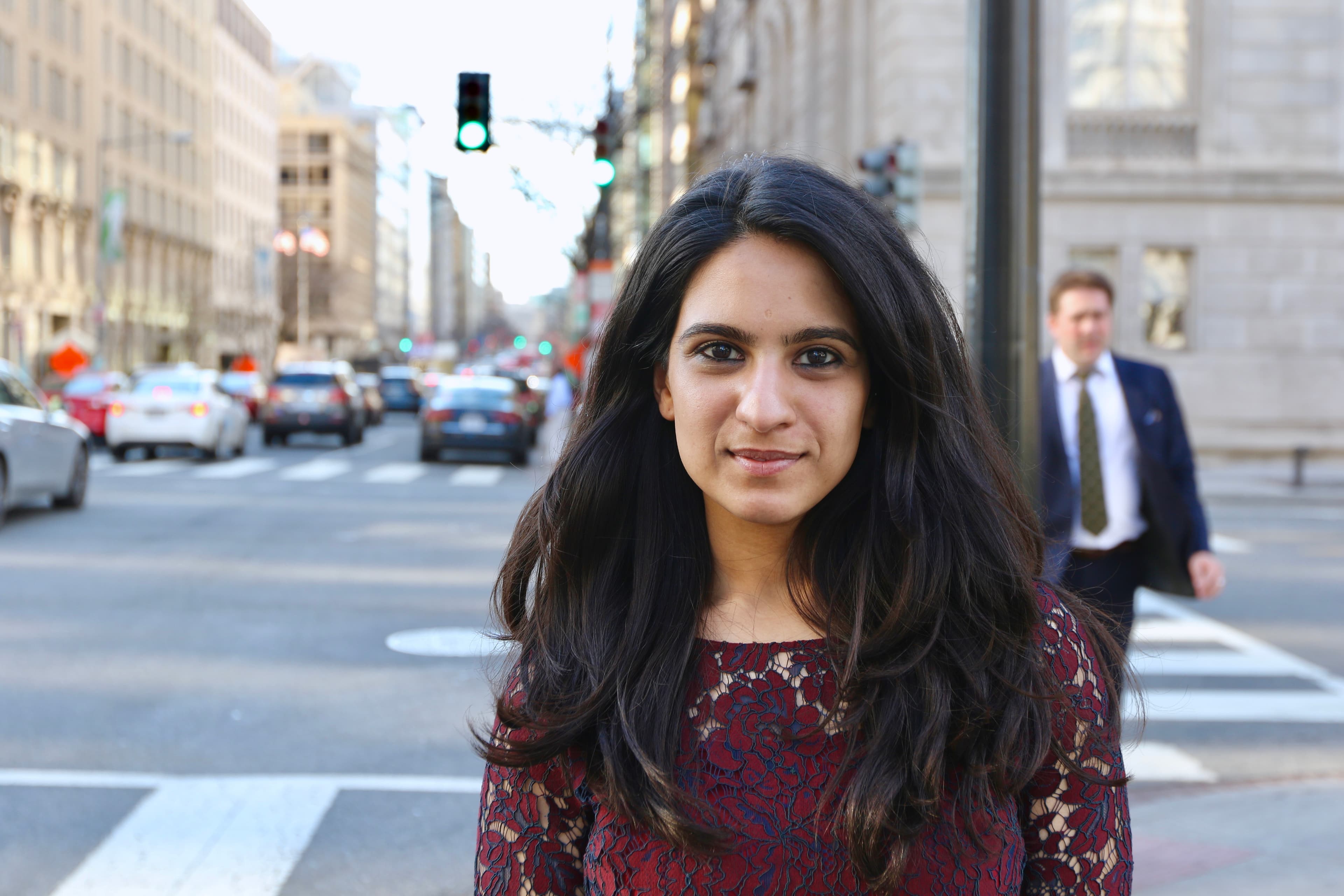A woman standing on street looks at the camera and smiles.