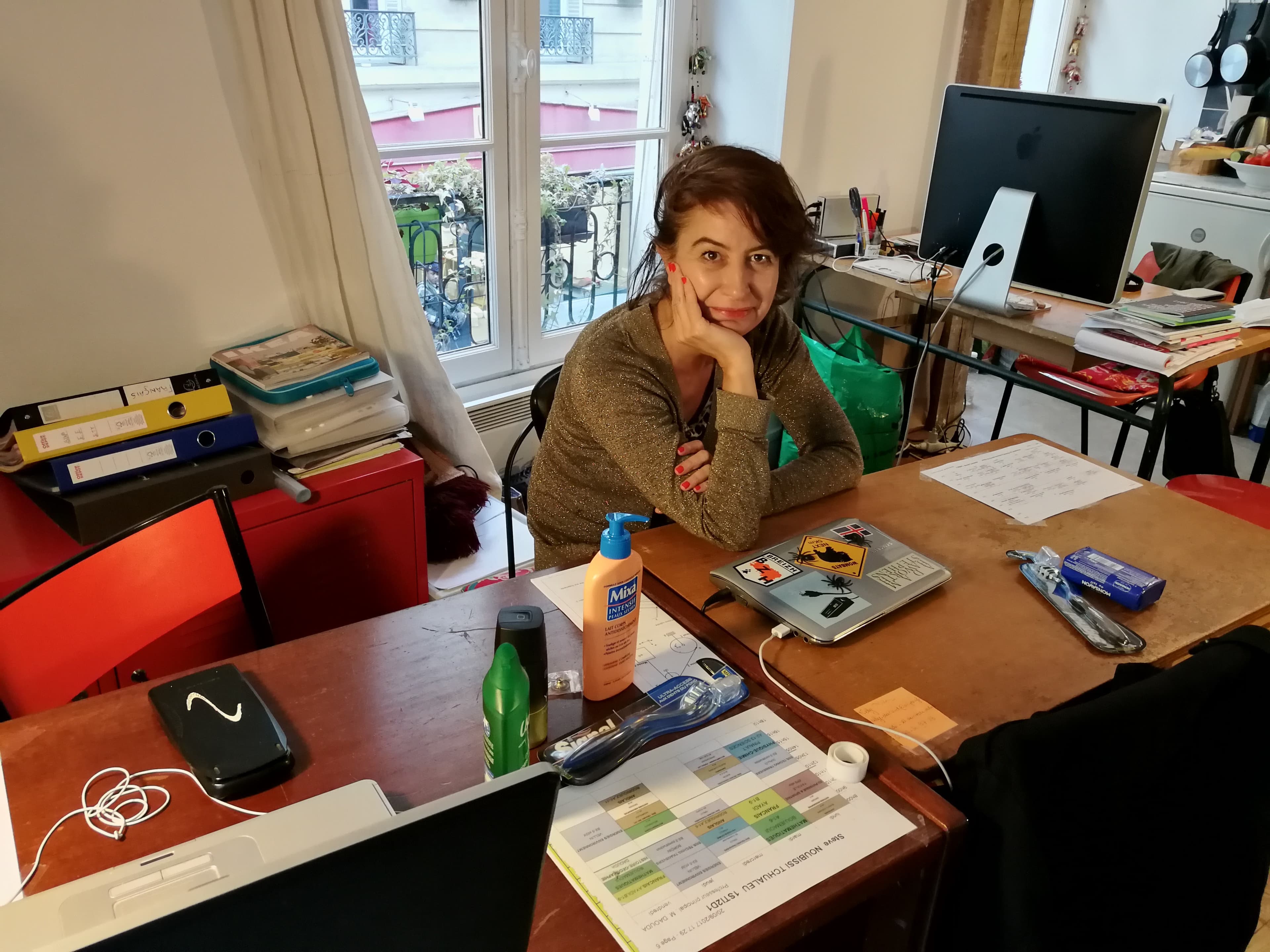 A woman sits at a desk with a window behind her.