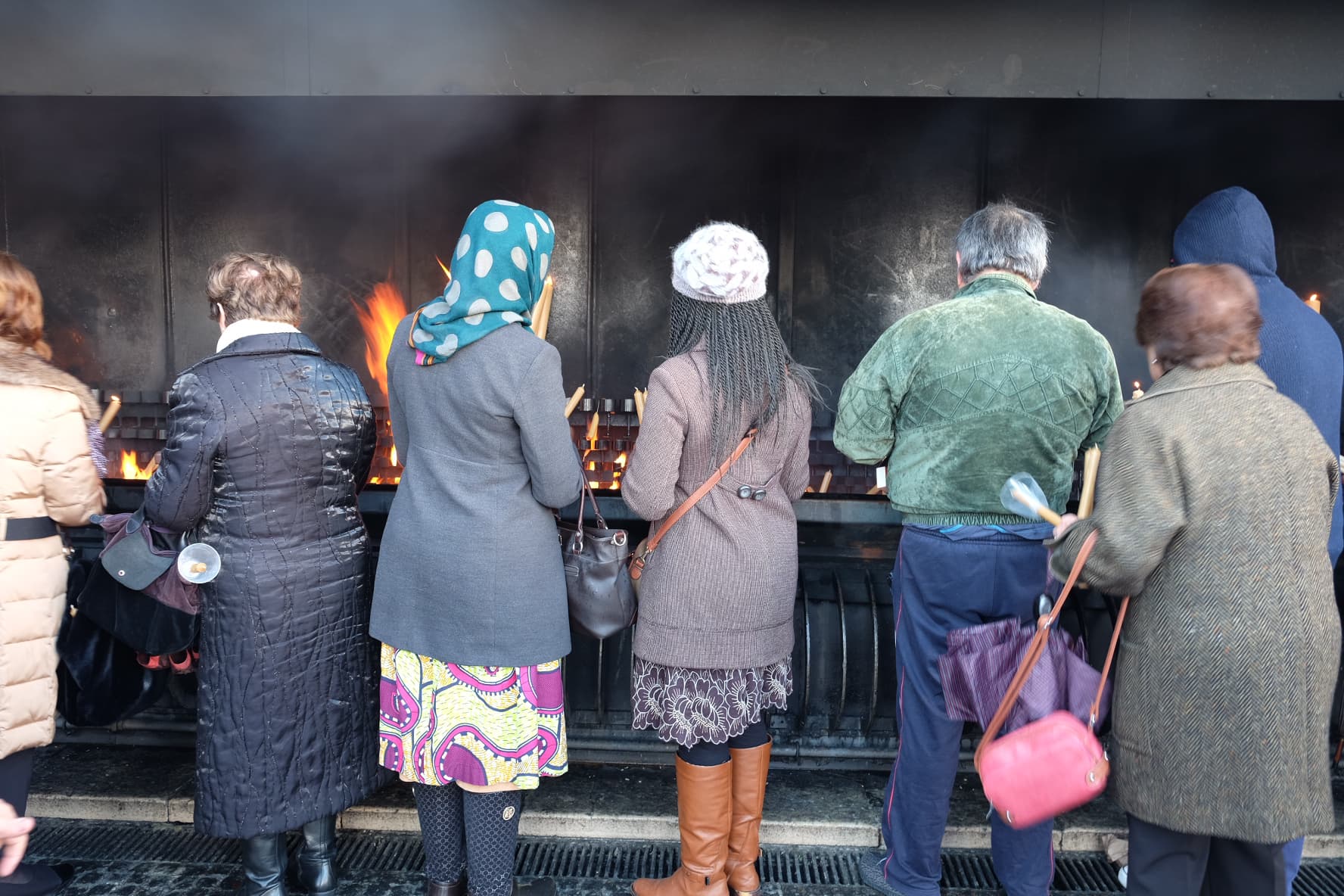A line of people burning candles and wax figures over a fire pit outside the Shrine of Fatima.
