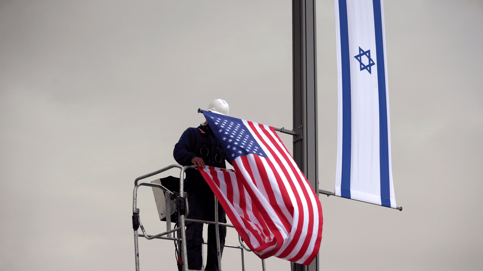 A worker on a crane hangs a US flag next to an Israeli flag, next to the entrance to the US consulate in Jerusalem, May 7, 2018.