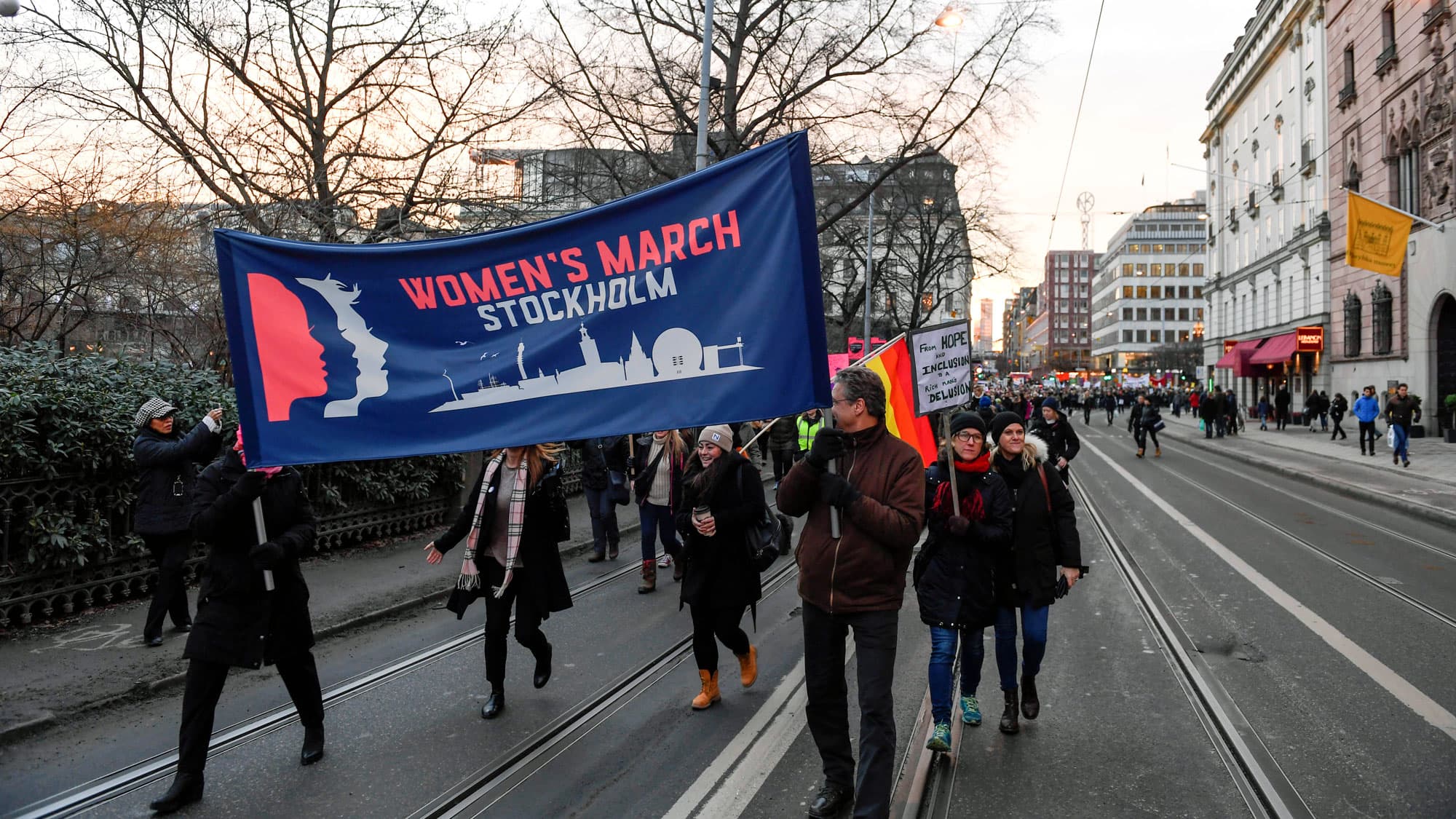 People carry a large banner that says "Women's March Stockholm" down a wide city street.