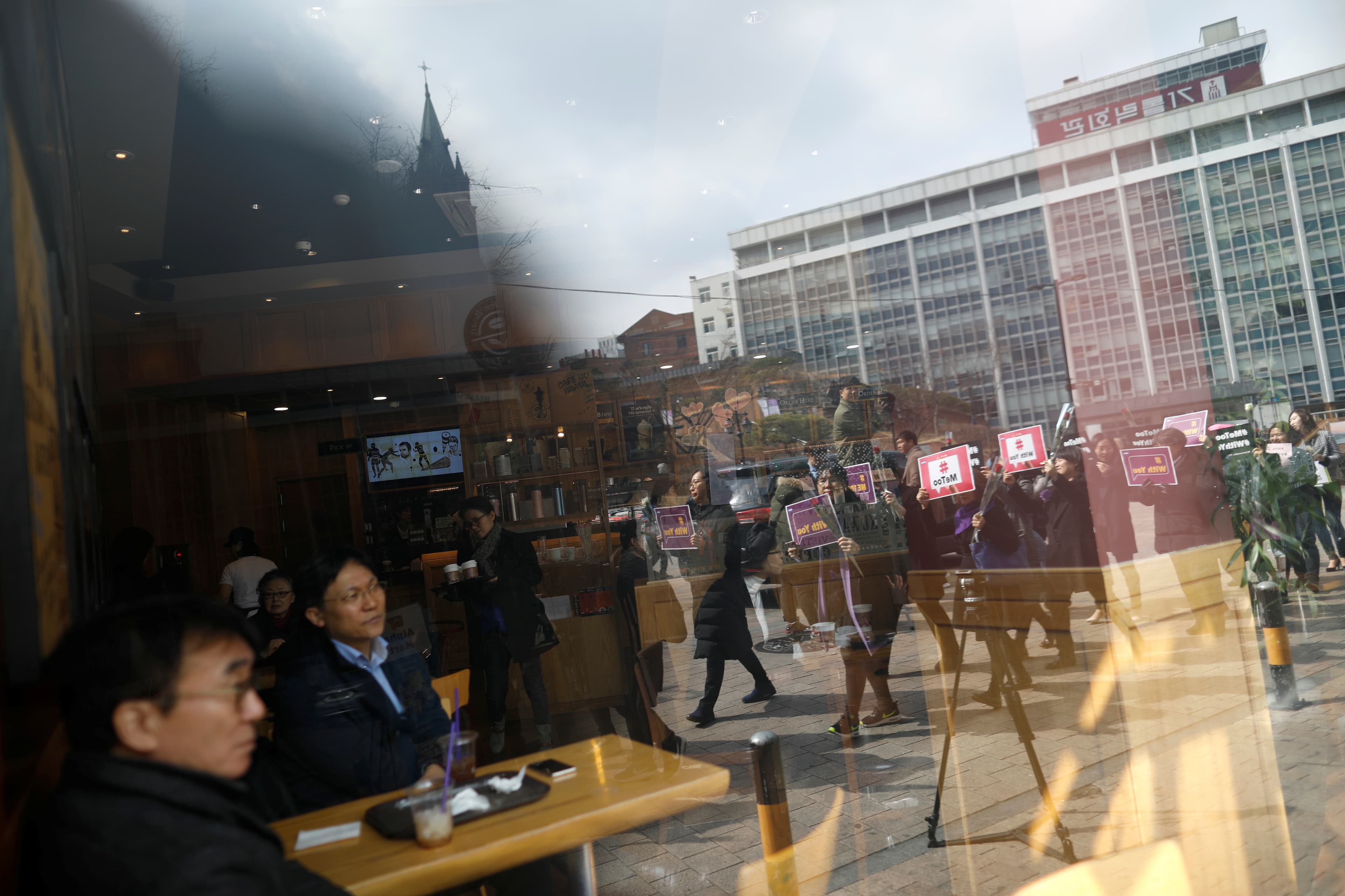 Women marching on a street are reflected on a window of a cafe