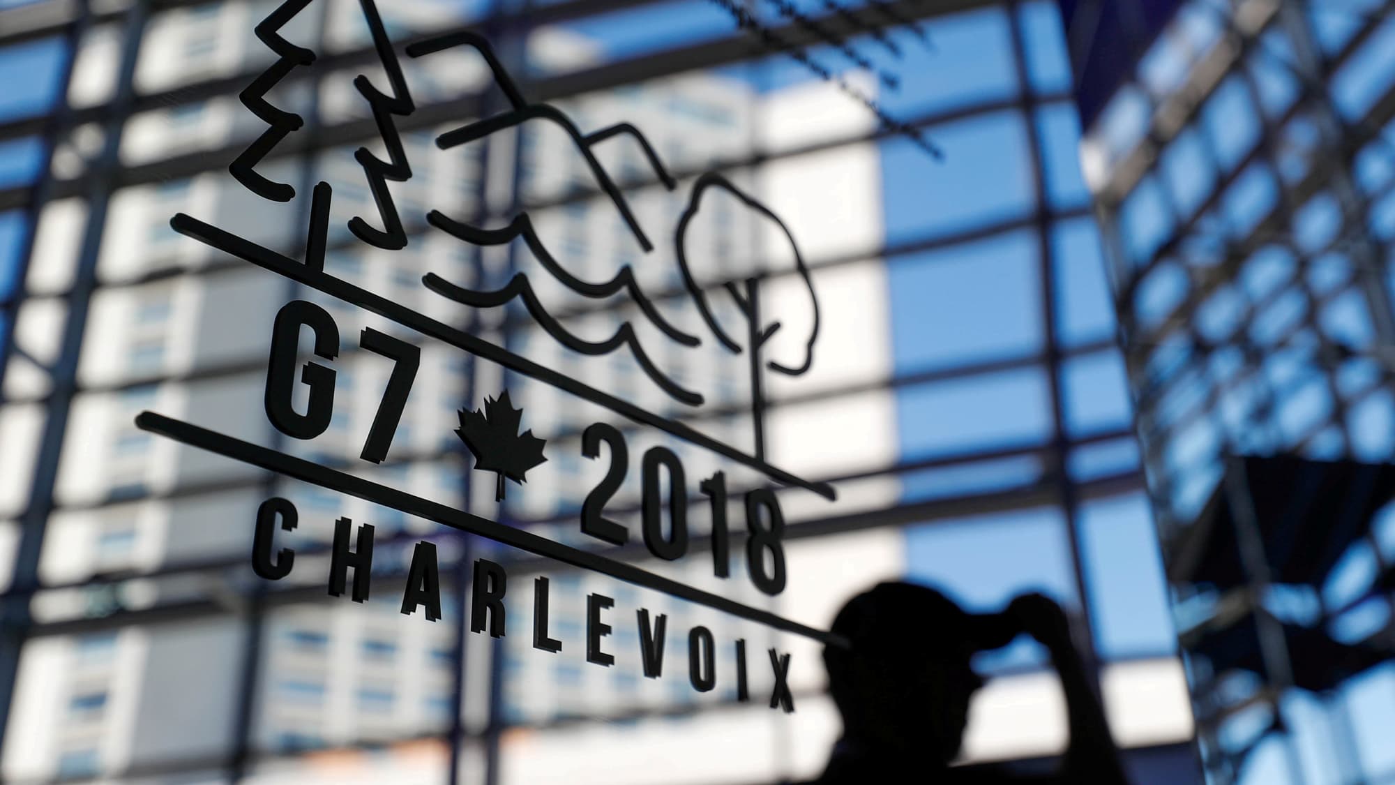 A man walks past the mirrored Charlevoix G7 logo in shadow in Quebec.
