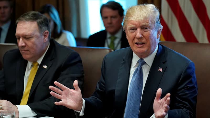 US President Donald Trump is seen sitting at a table with his hands outstretched with other cabinet officials sitting adjacent.