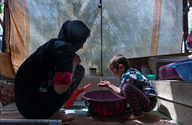 A woman and young child squat around a bowl of water