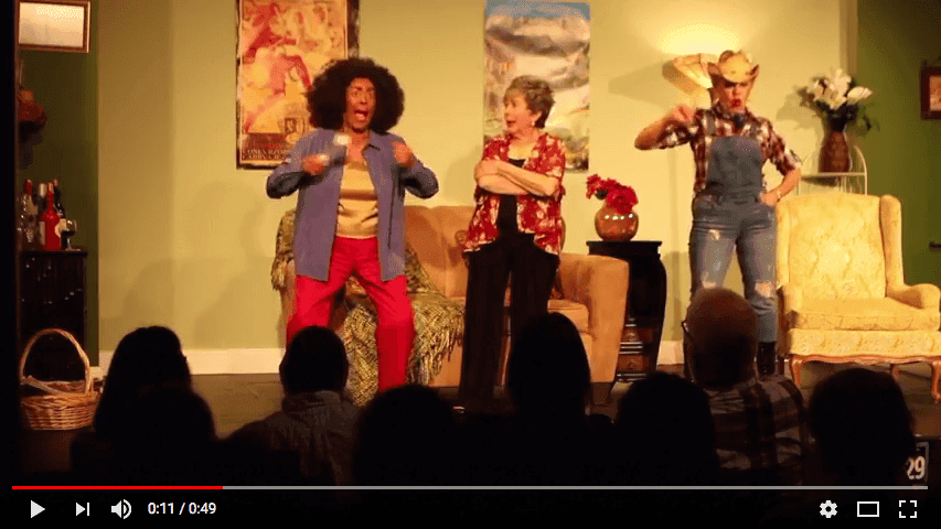 Three women on stage gesticulating, one with blackface pounding her chest