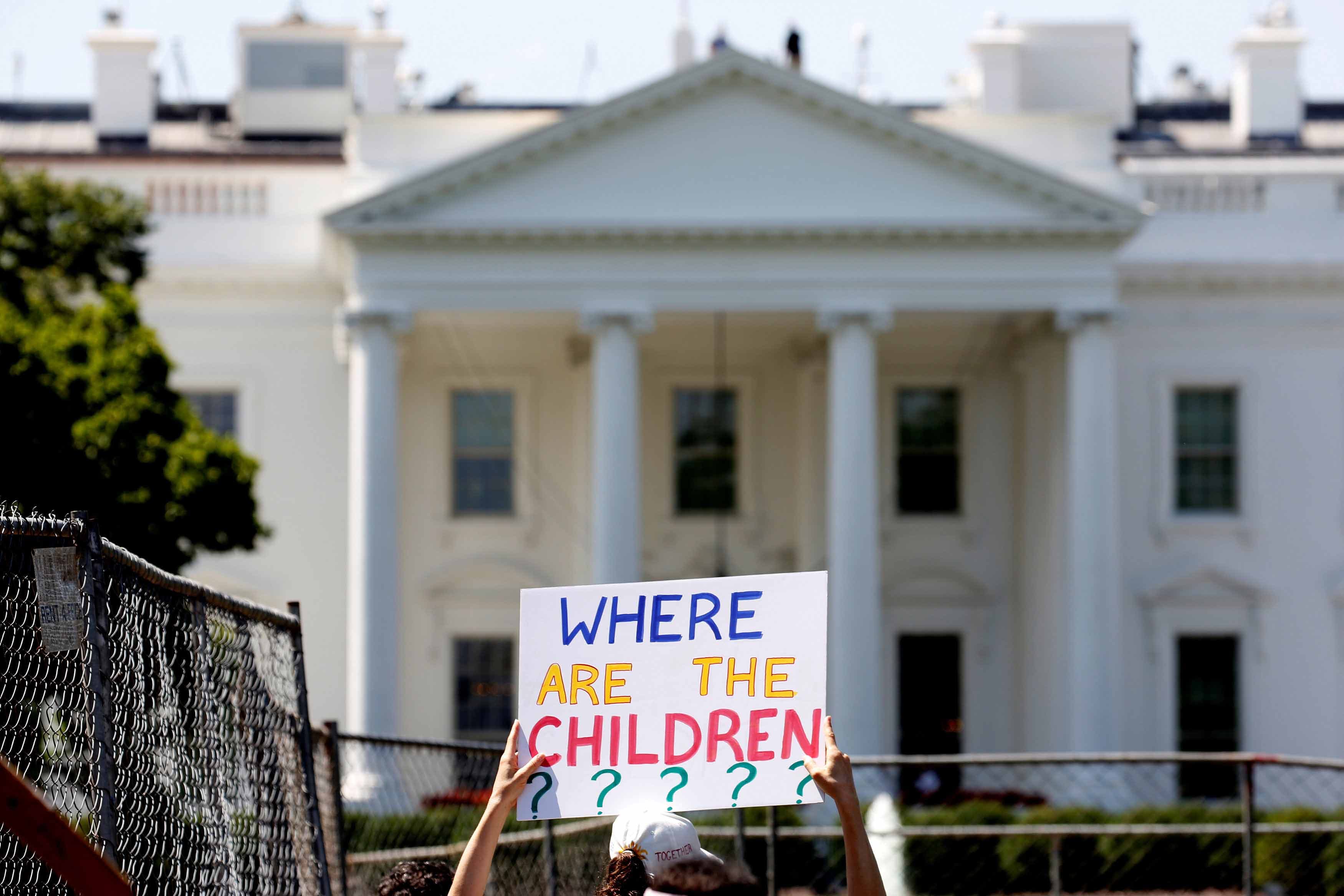 A protester holds a sign in front of the White House that says 